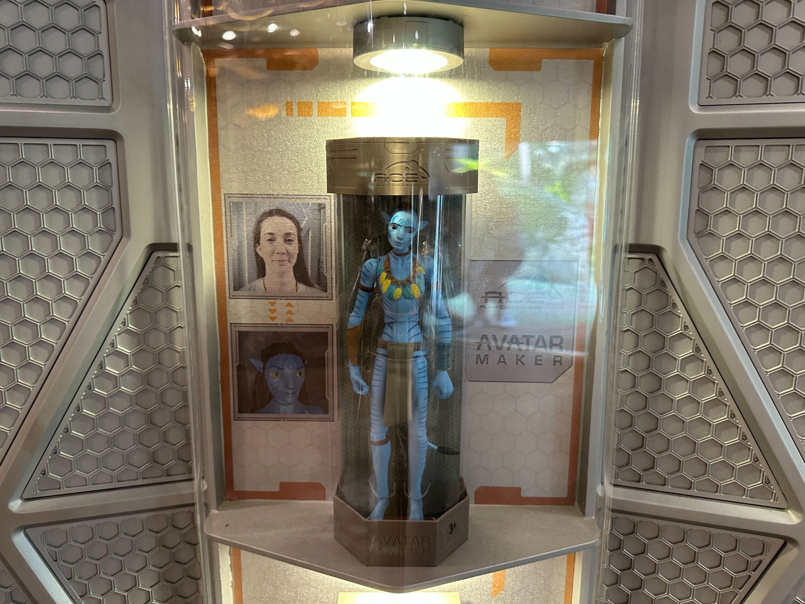 A blue Na’vi action figure is displayed in a case with photos showing the transformation process beside it.