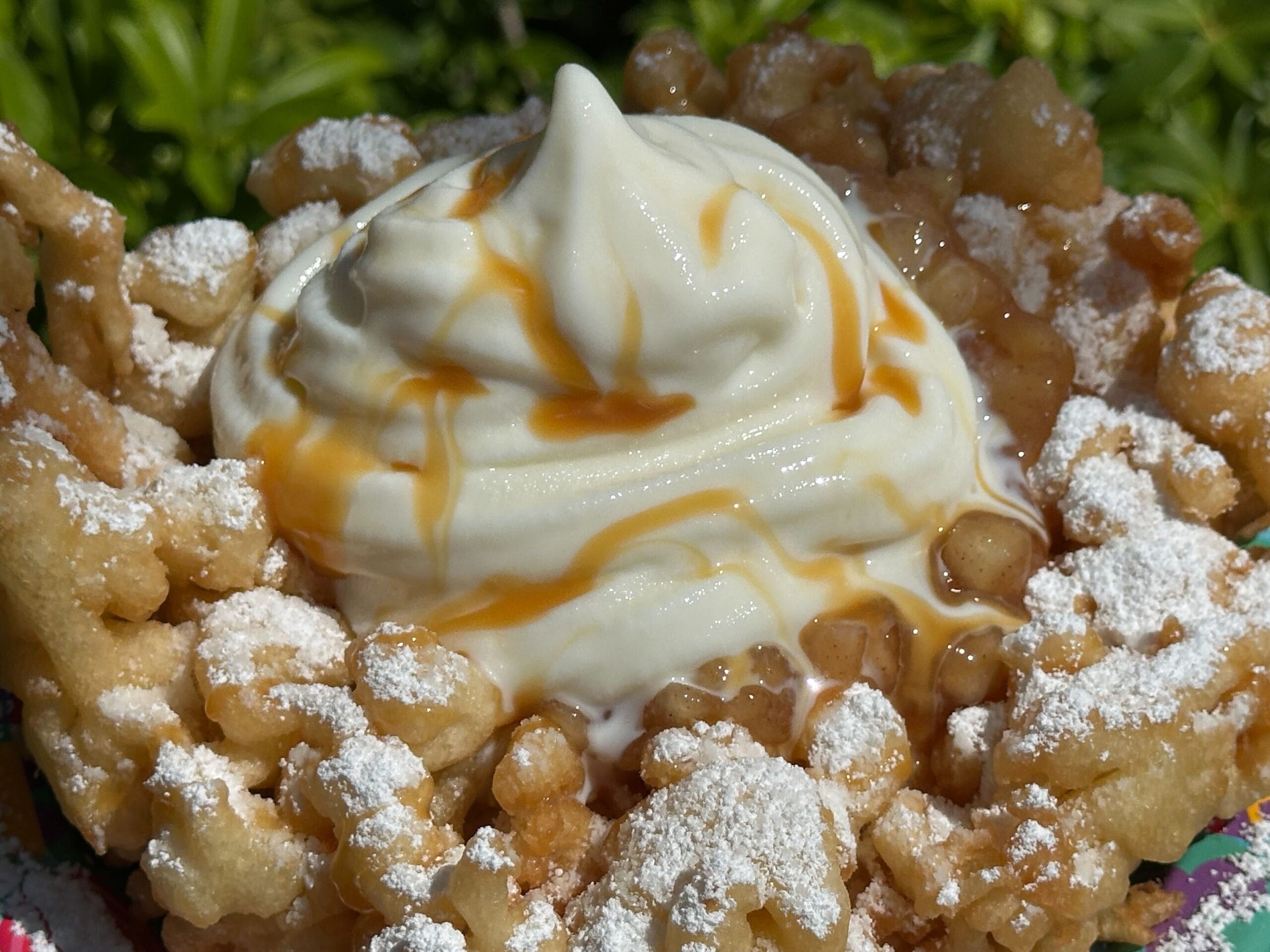 An Apple Pie Funnel Cake topped with soft serve vanilla ice cream, caramel drizzle, and powdered sugar.