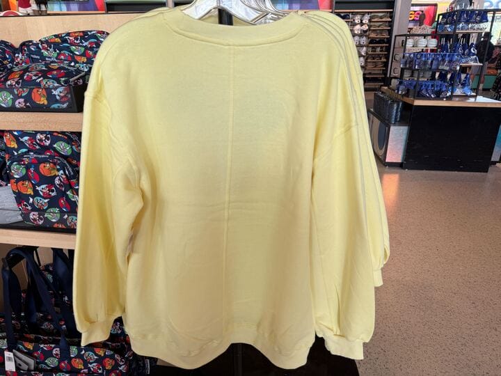 A plain light yellow long-sleeve Character Sweatshirt hanging on a rack in a store.