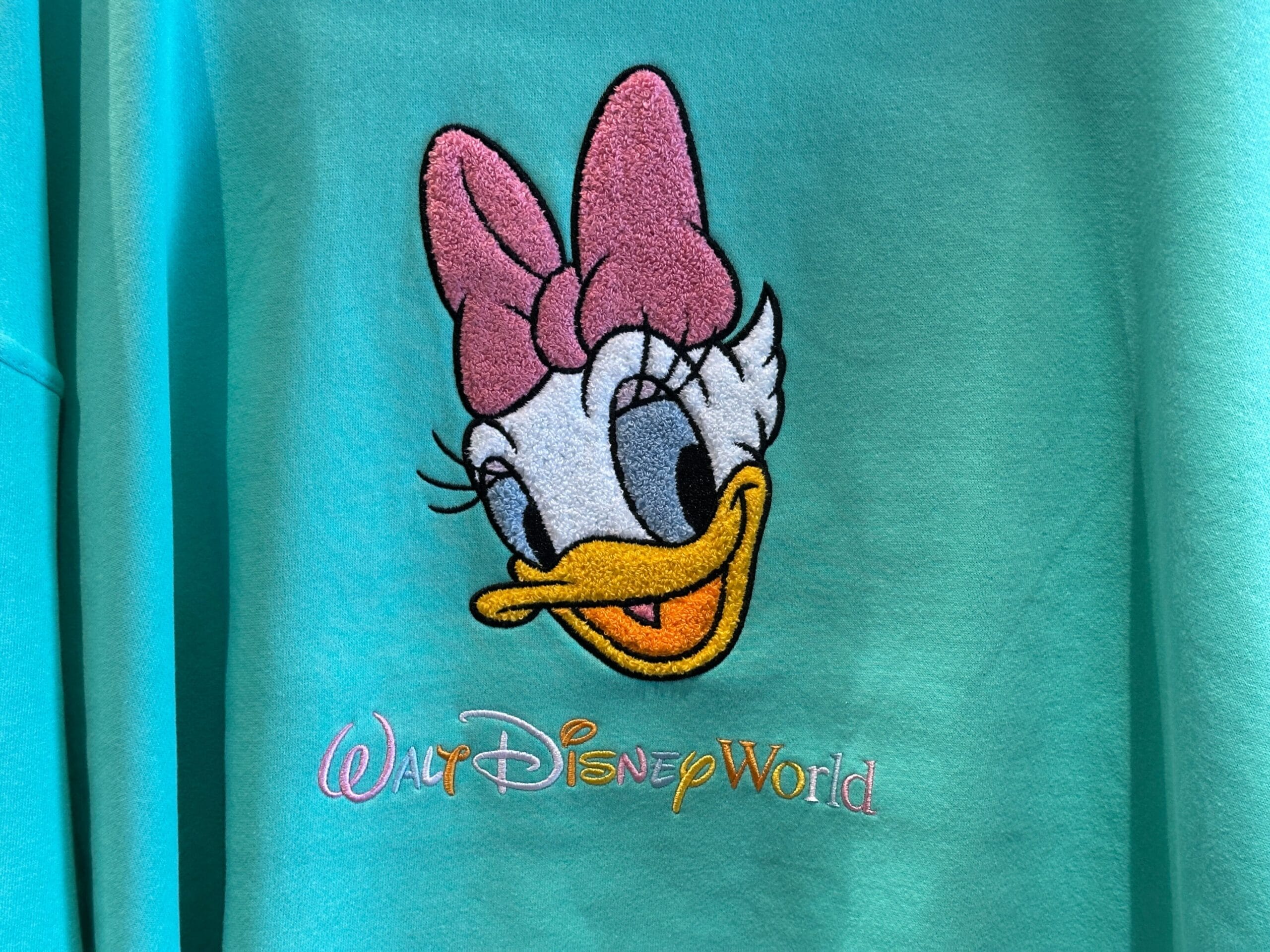 A teal shirt from the New Arrivals features Daisy Duck's face above "Walt Disney World" embroidered in colorful letters.