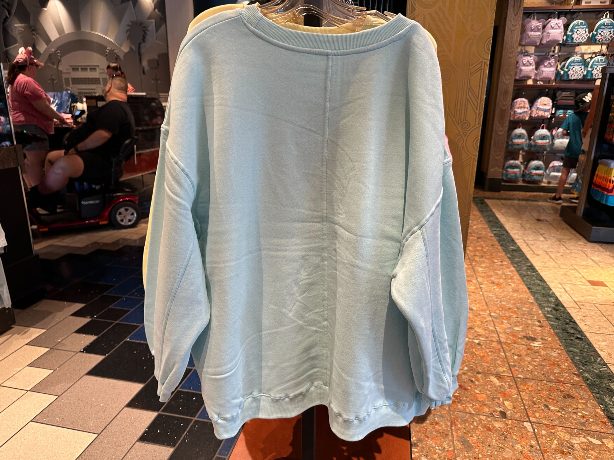 A light blue long-sleeve Walt Disney World sweatshirt hanging on a rack in a retail store.
