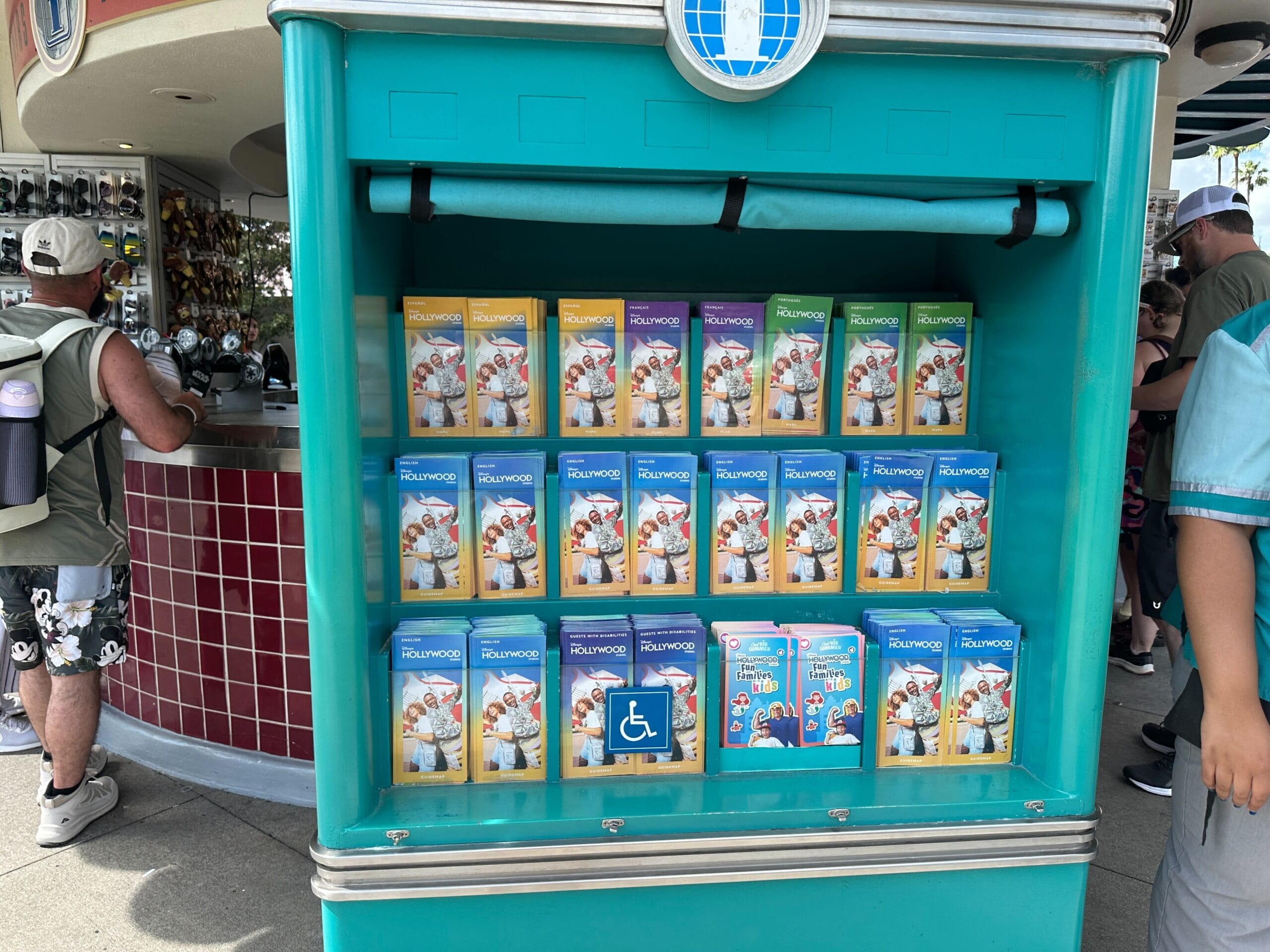 Display rack with colorful collectible cards, a guidemap, and MuppetVision 3D card near a blue wheelchair accessibility sign.