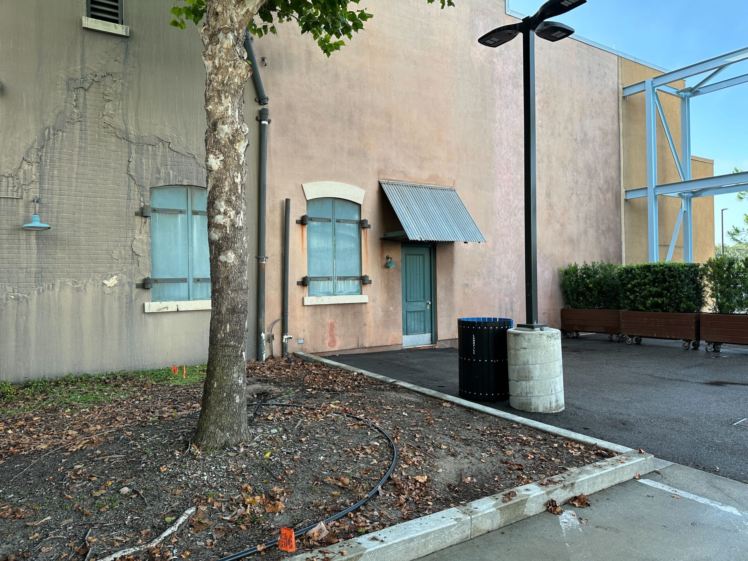 A weathered building with blue shutters and door, benches, and a tree evokes the charm of MuppetVision 3D.