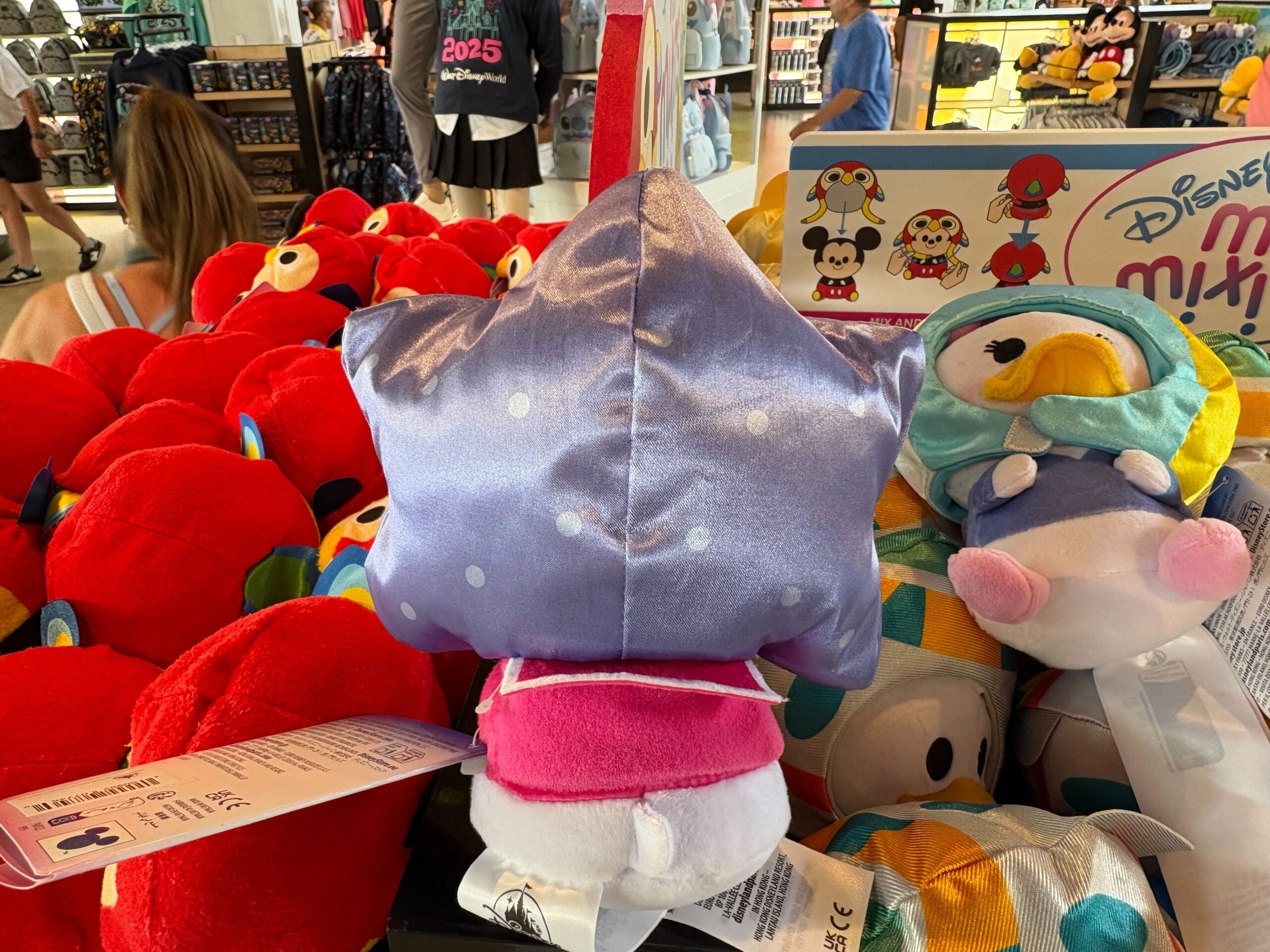 Plush toys, including a purple star with polka dots, displayed on a store shelf with other colorful stuffed animals.