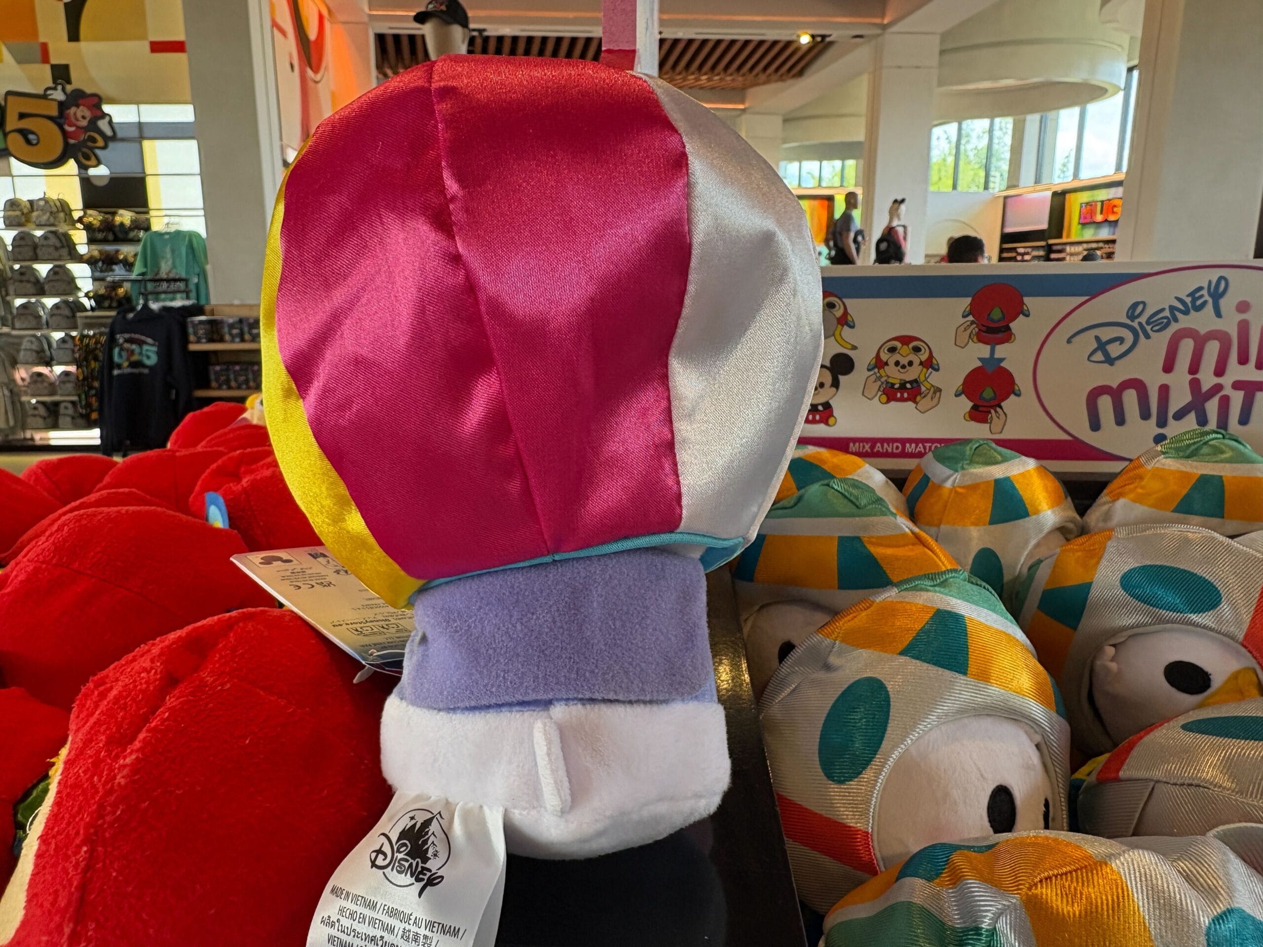Colorful plush toy shaped like a crown on display in a Disney store with other plush toys in the background.