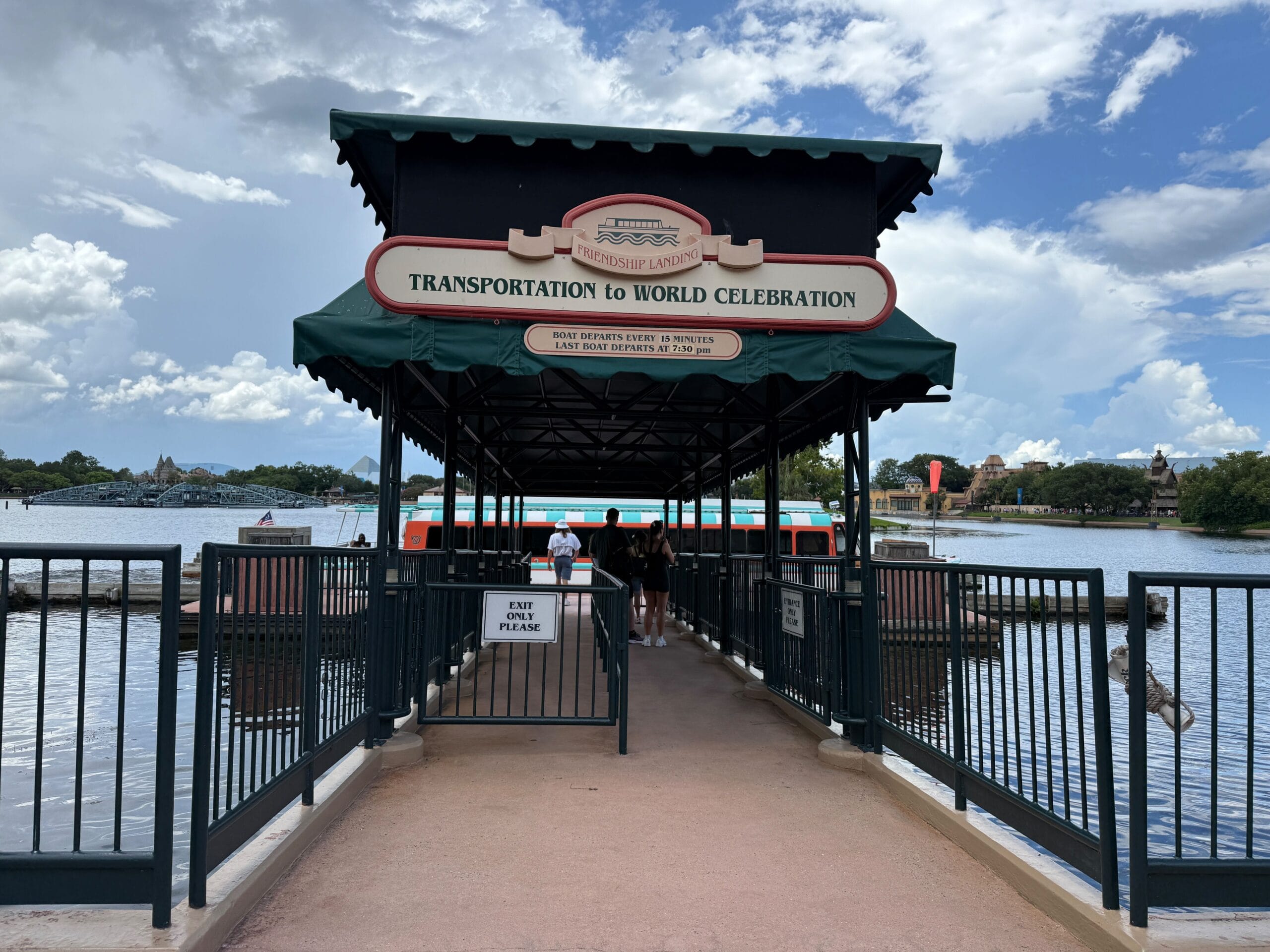 Covered boat dock for Friendship Boats labeled "Transportation to World Celebration," with people boarding under blue sky.