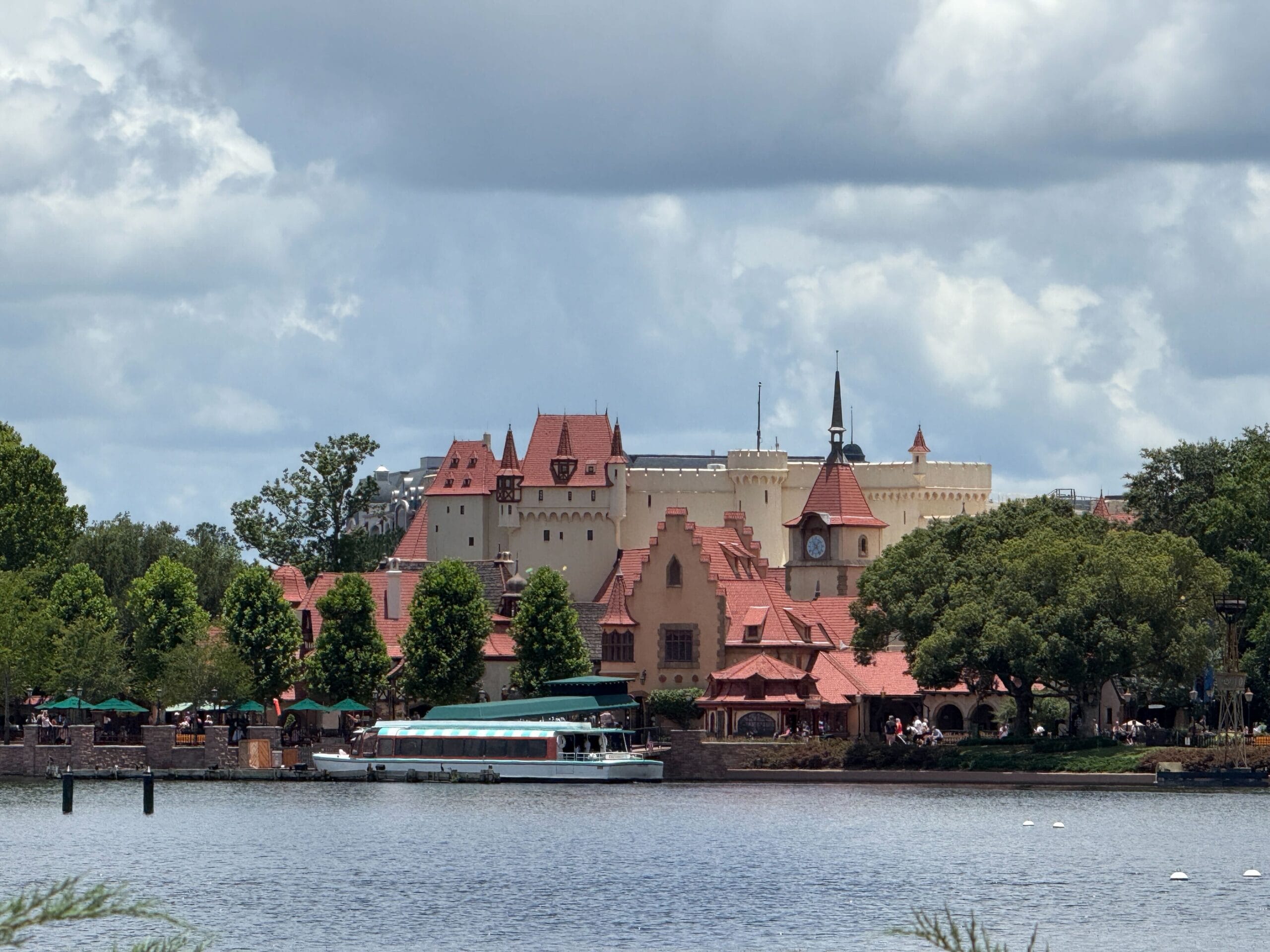 A scenic waterfront view of German-style buildings with red roofs and Friendship Boats docked under a cloudy sky.