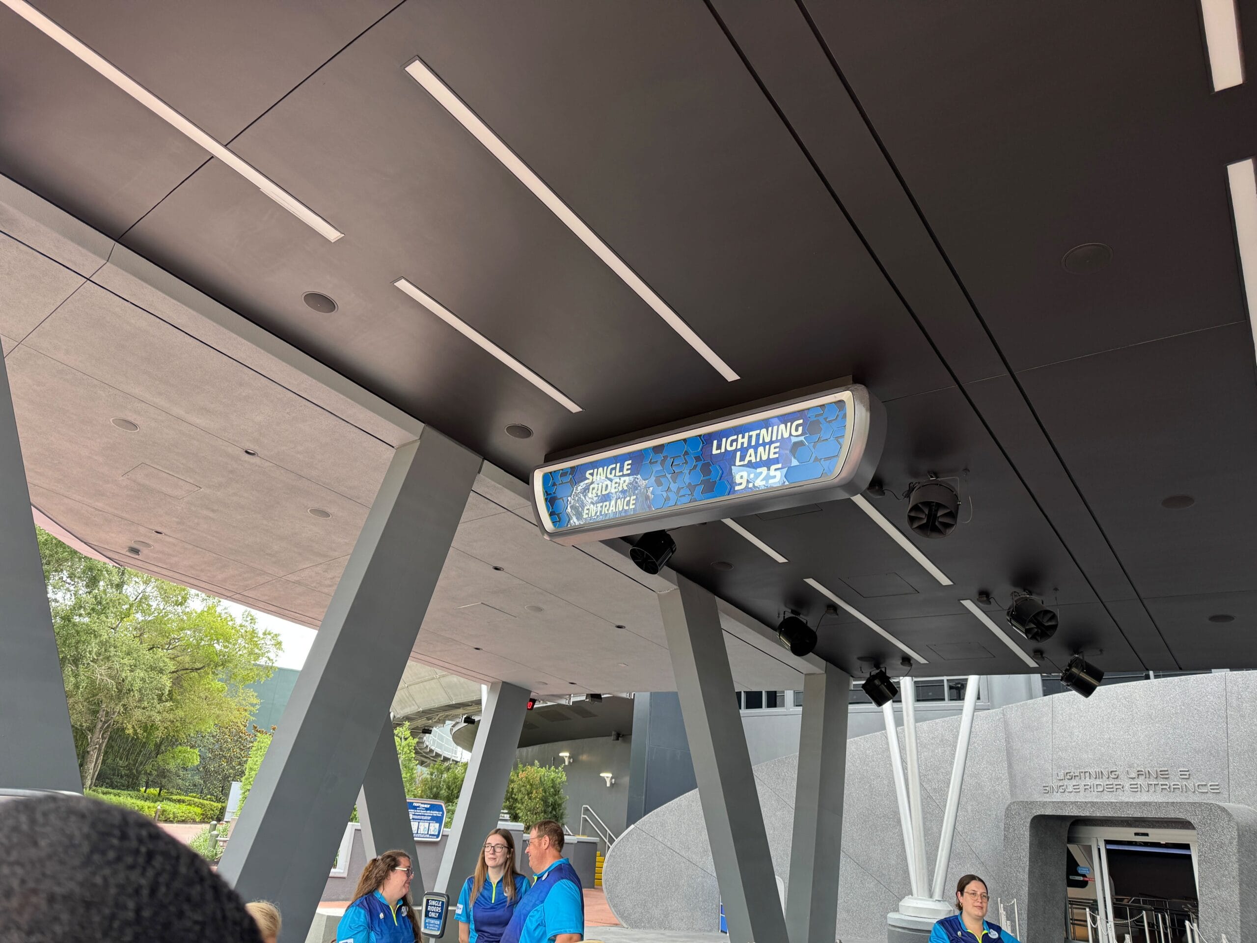 Outdoor entrance to Test Track with a digital sign showing Lightning Lane time and staff members standing below.