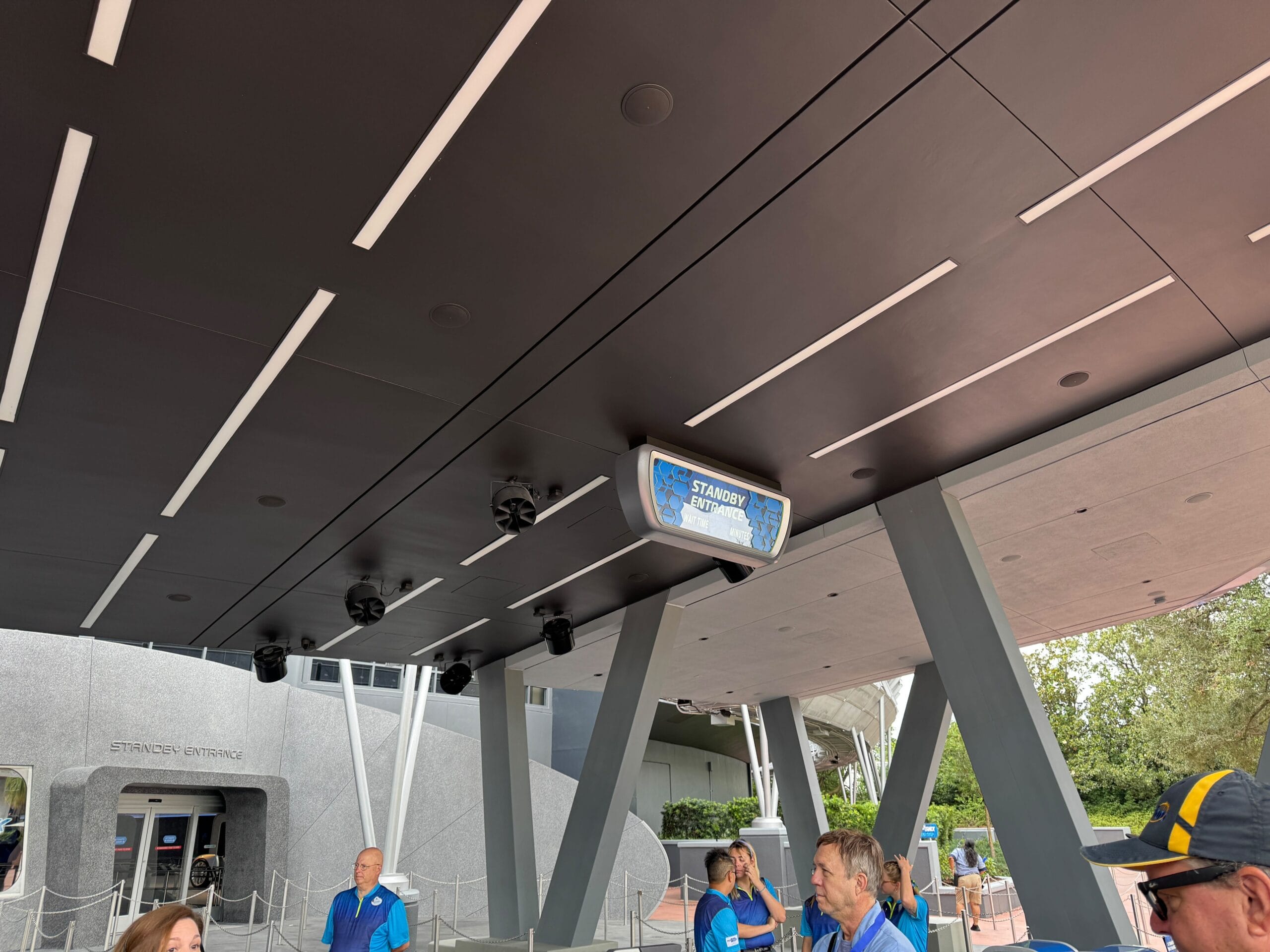 People stand under a covered "Standby Entrance" sign, waiting to enter the Test Track 3.0 attraction or building.