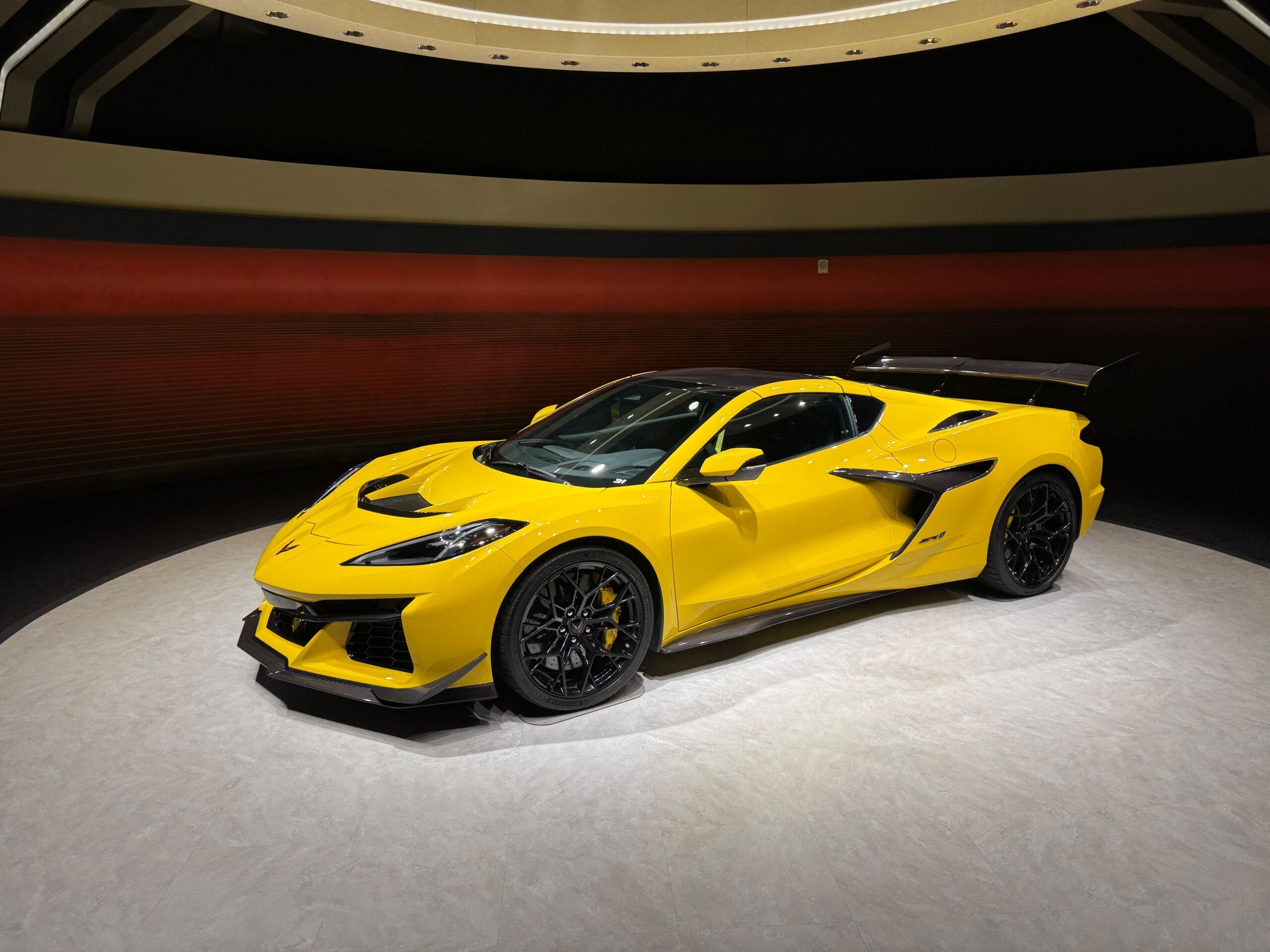 A bright yellow sports car with a large rear spoiler dazzles under spotlights on Test Track 3.0’s circular platform.