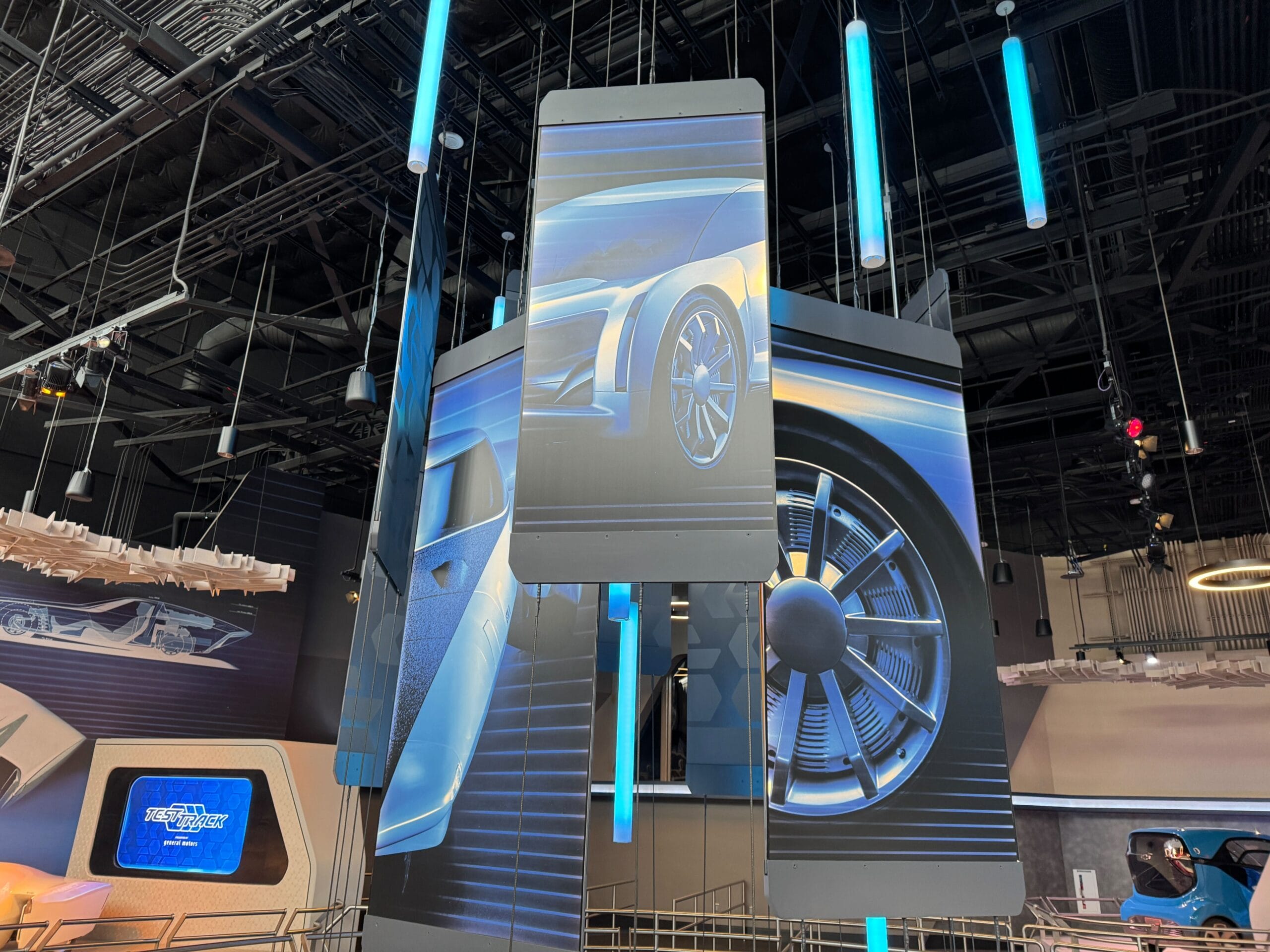 Large panels display futuristic car designs in a modern indoor Test Track setting with blue vertical lights.