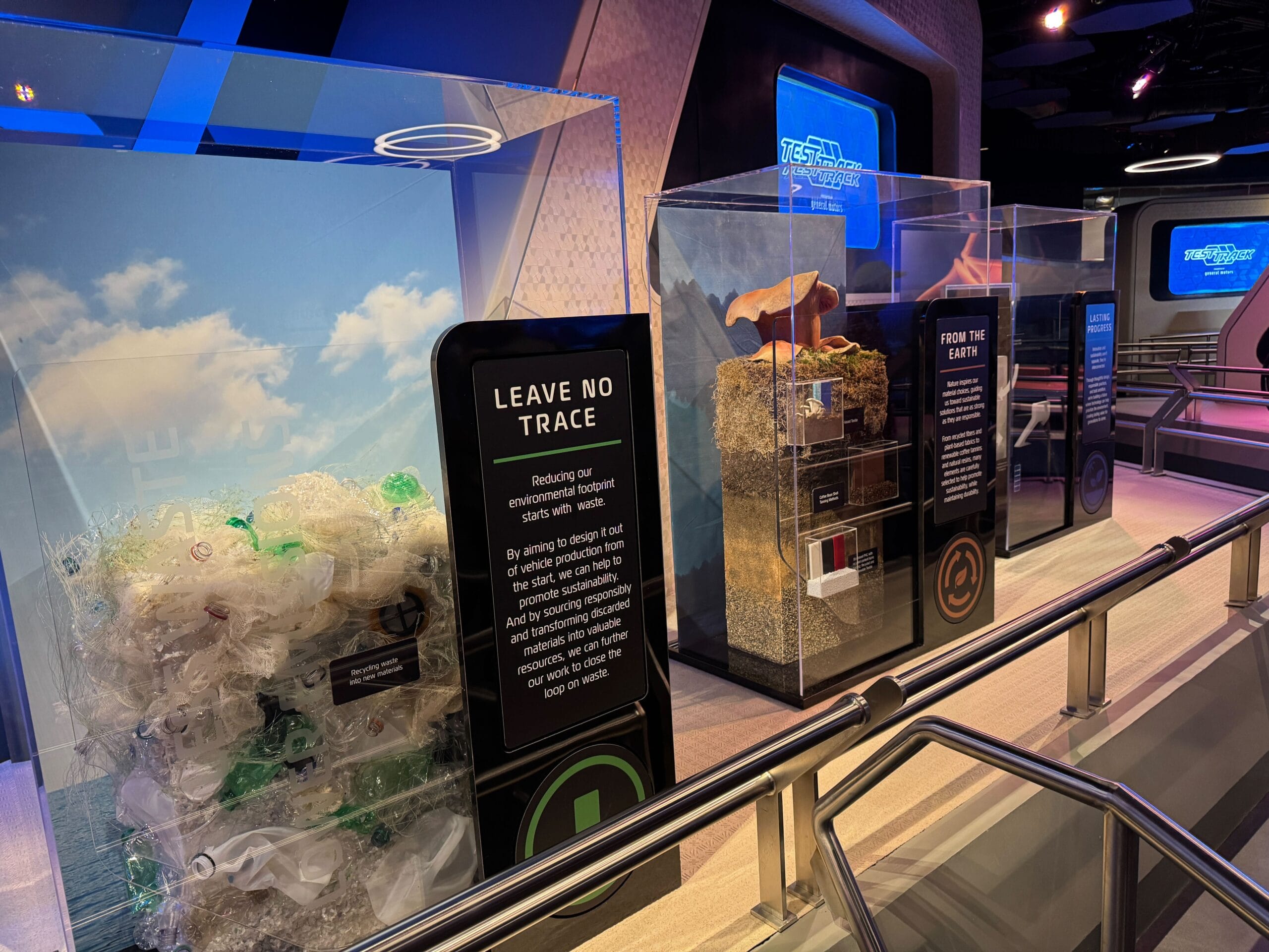 Exhibit displays about reducing environmental waste, featuring Test Track-inspired cases with plastic behind glass.