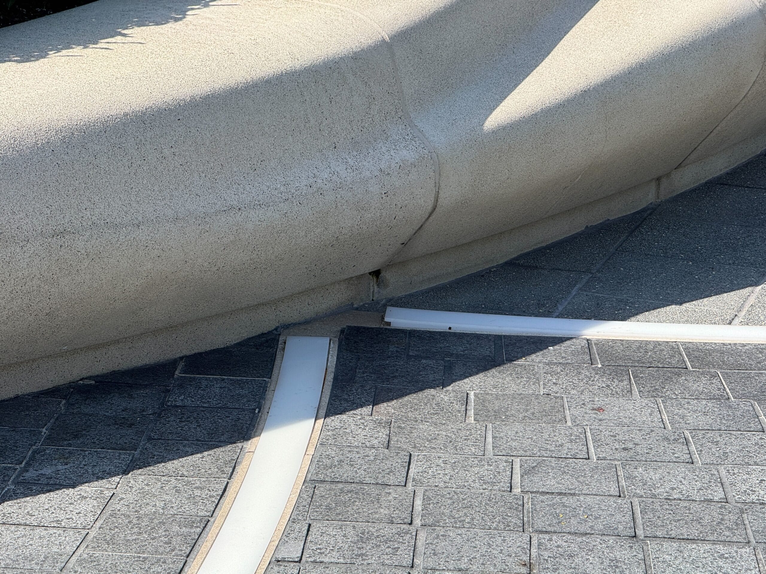 Curved stone bench with a crack near the base, bordered by gray bricks and white strips on the ground.