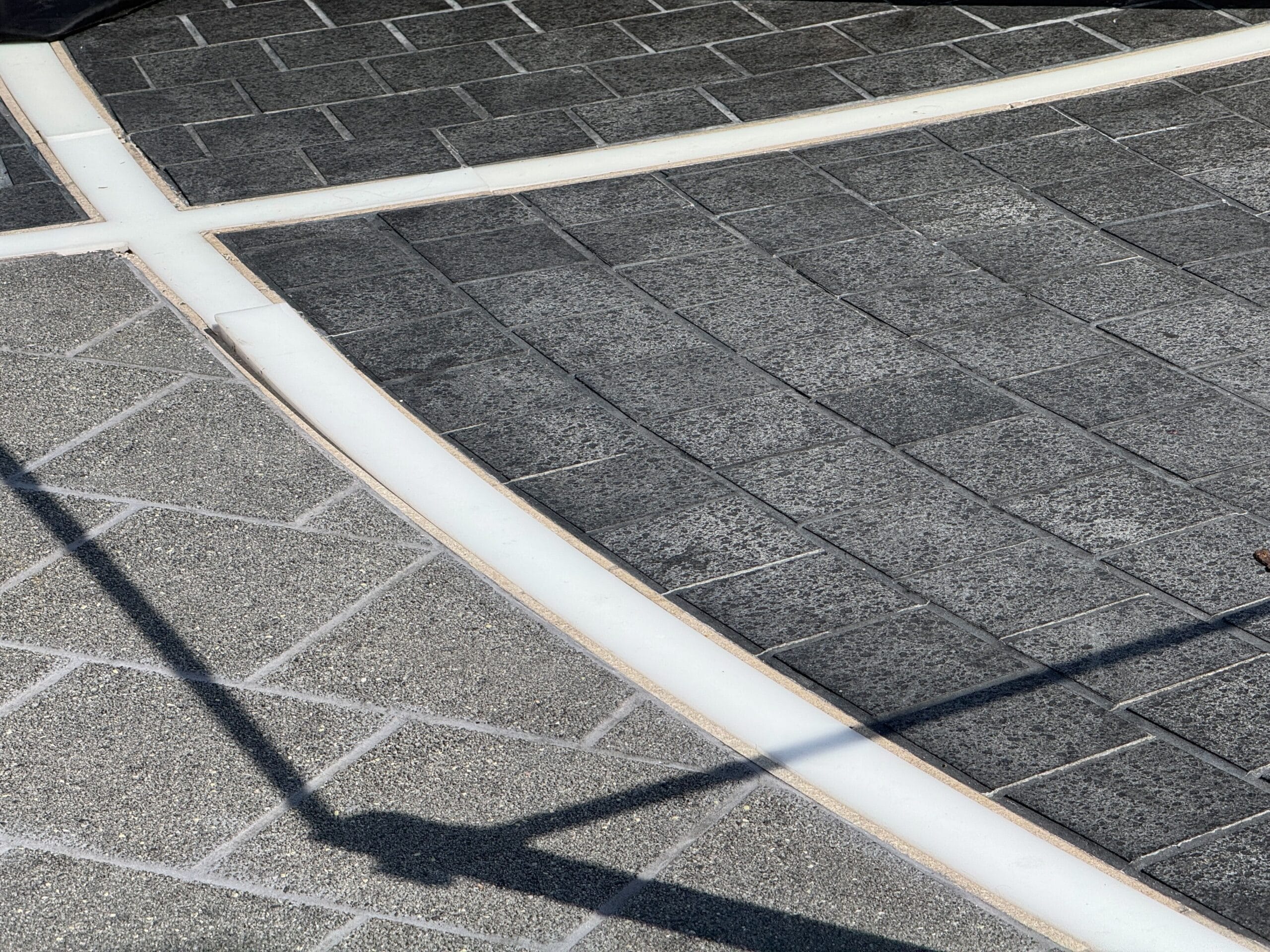 Gray stone pavement with intersecting white lines and a shadow, reminiscent of EPCOT’s World Celebration Light-Up Pavement.