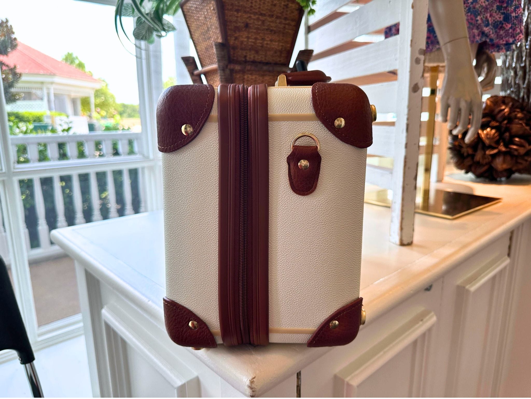 Small vintage-style mini luggage bag with brown trim sits on a white counter near a window display.
