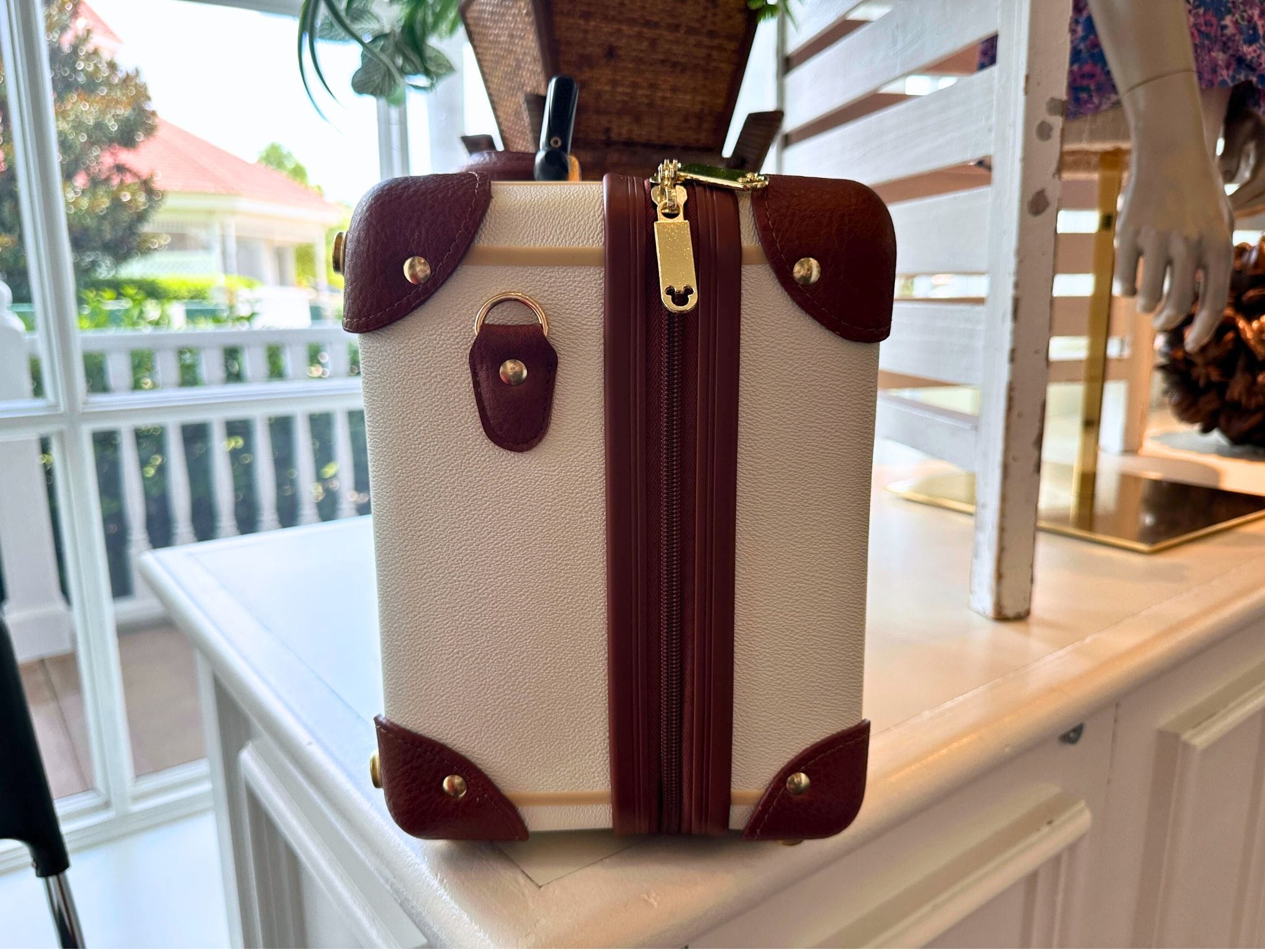 A small white and brown mini luggage bag with a zipper sits on a white counter indoors.