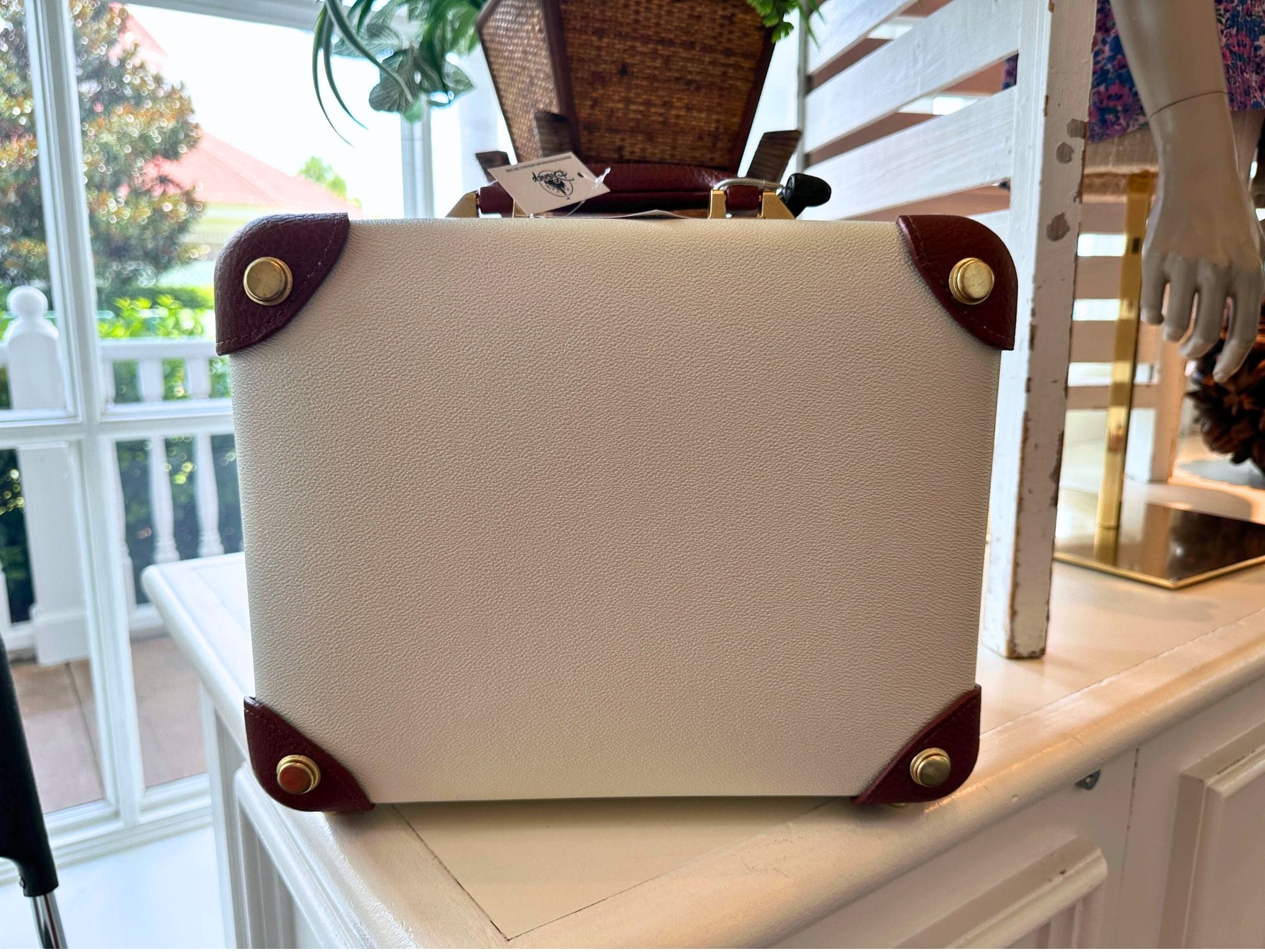 A mini luggage bag with brown corners and gold studs sits on a white shelf, evoking Disney's Grand Floridian Resort.