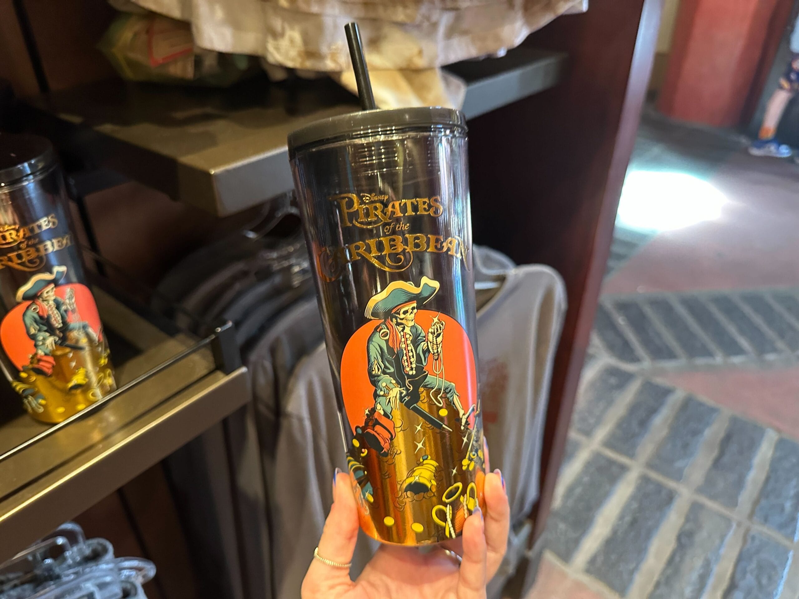 A hand holds a Pirates of the Caribbean tumbler featuring a skeleton pirate and treasure chest design.
