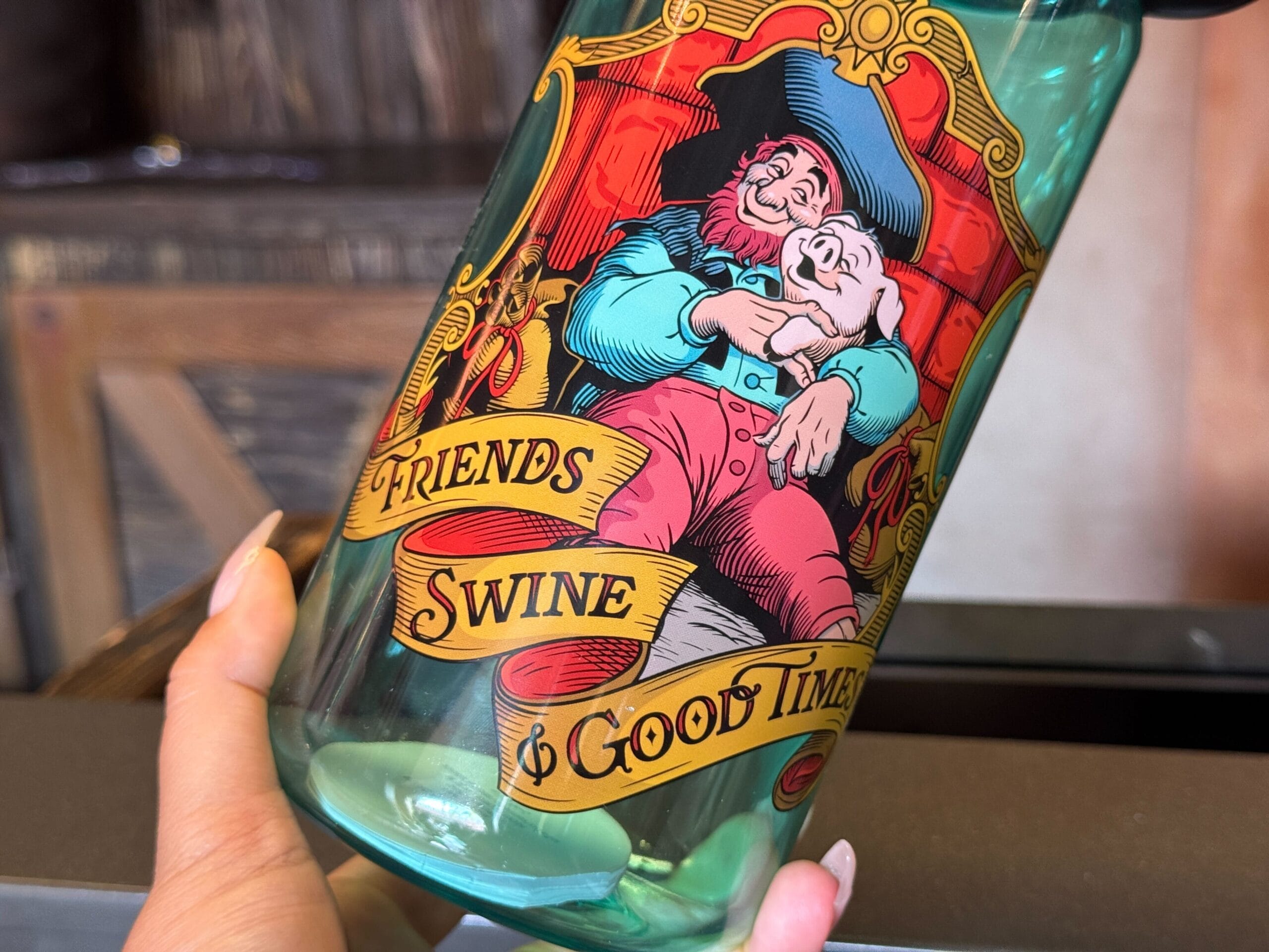 A hand holds a bottle with a cartoon pirate hugging a pig and text reading "Friends, Swine & Good Times.