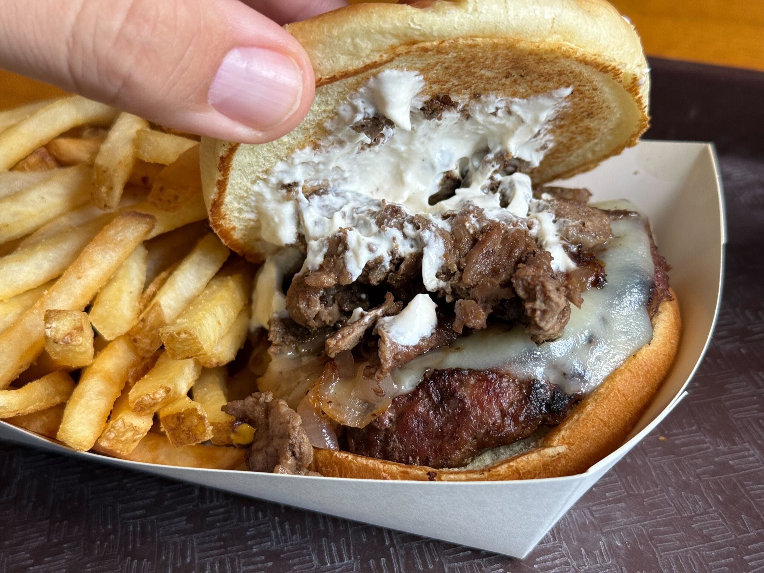 A hand lifts a burger bun at Disney's Port Orleans Resort, revealing beef, cheese, onions, sauce, and crispy fries.