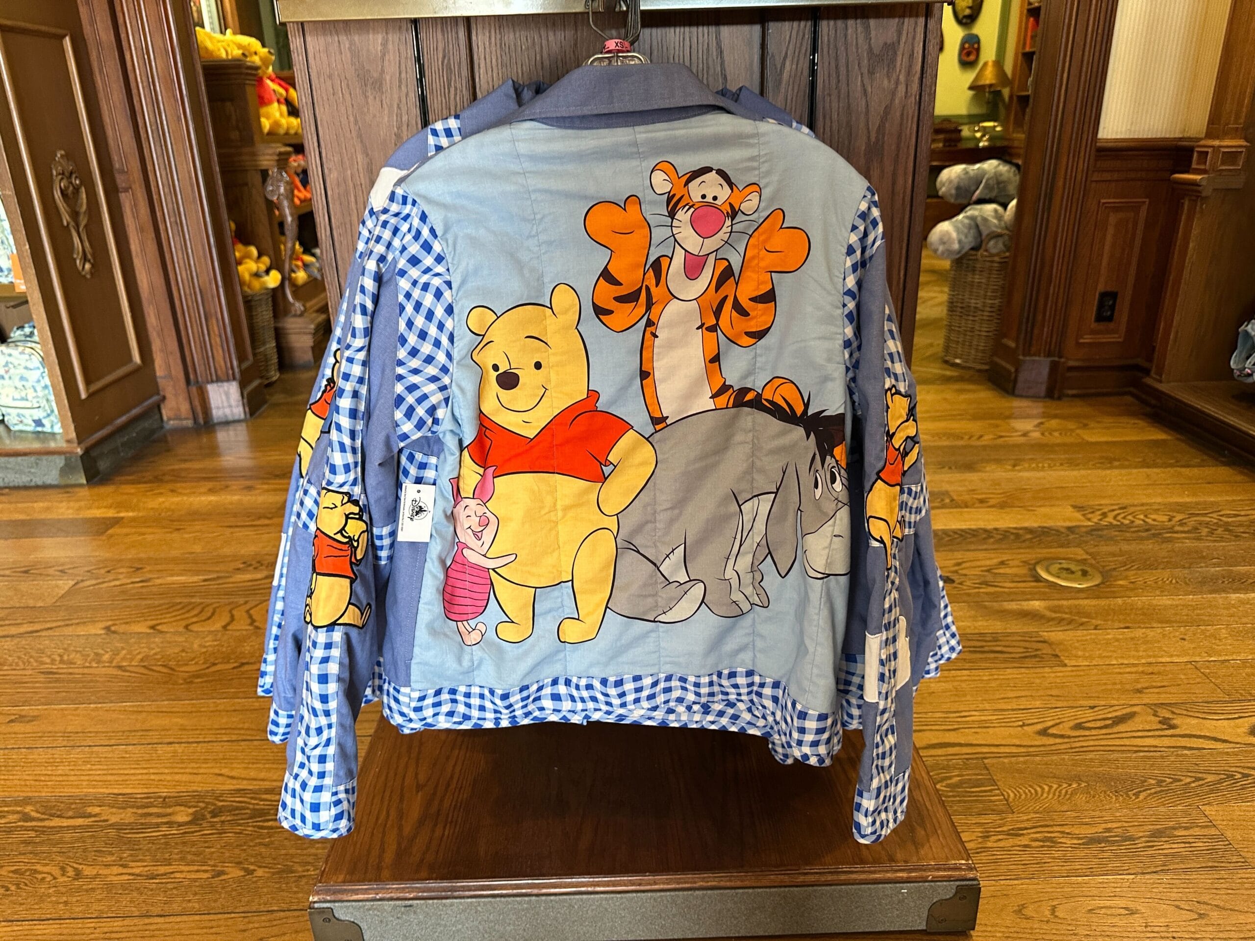 A winnie the pooh sweater with Piglet, Tigger, and Eeyore on the back, showcased in a store.