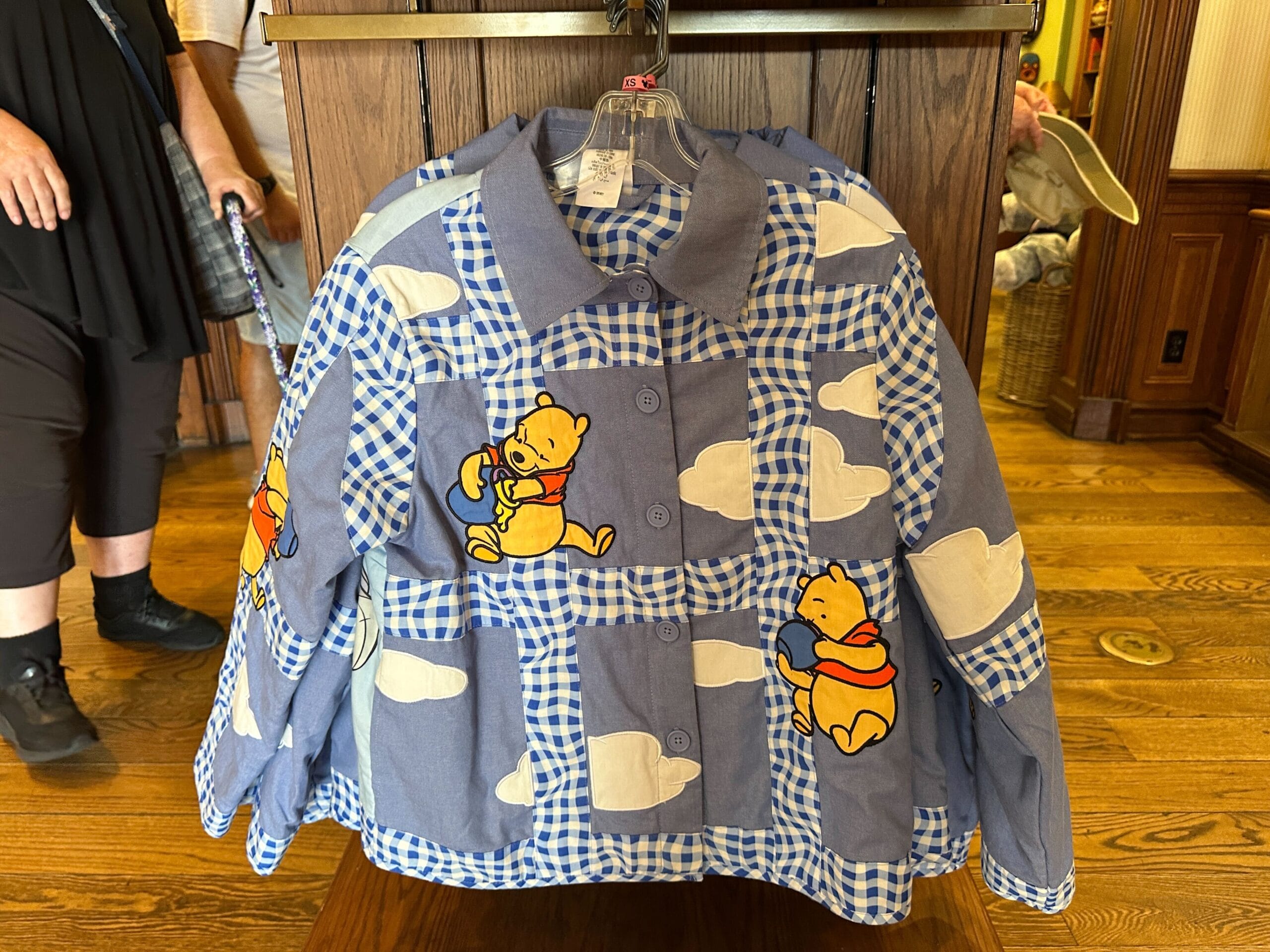 Blue and white checkered winnie the pooh sweater with clouds, displayed on a hanger in a store.