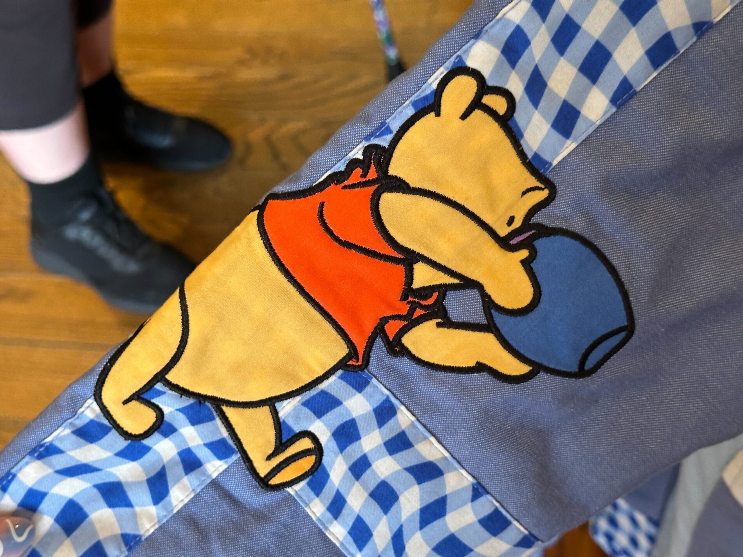 Patch of Winnie the Pooh in a red shirt holding a blue pot on blue checkered fabric, perfect for a Winnie the Pooh sweater.