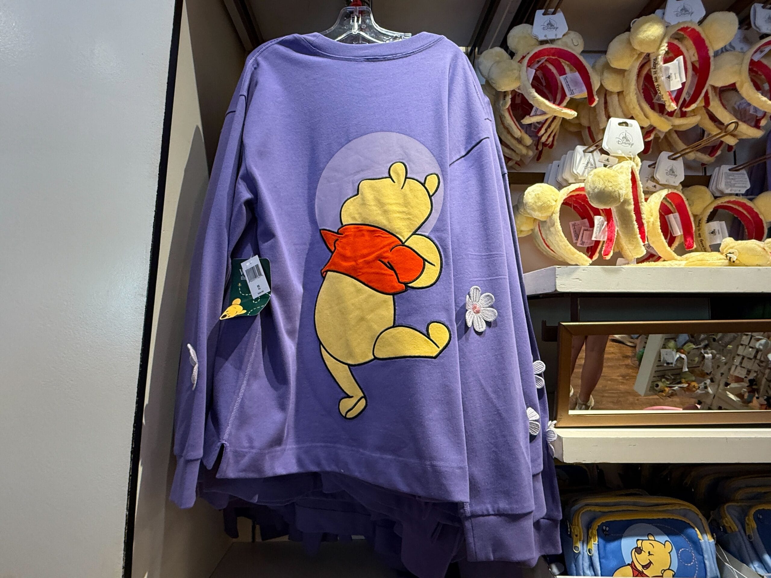 Purple winnie the pooh sweater with a red-scarved Pooh on the back, displayed in a store.