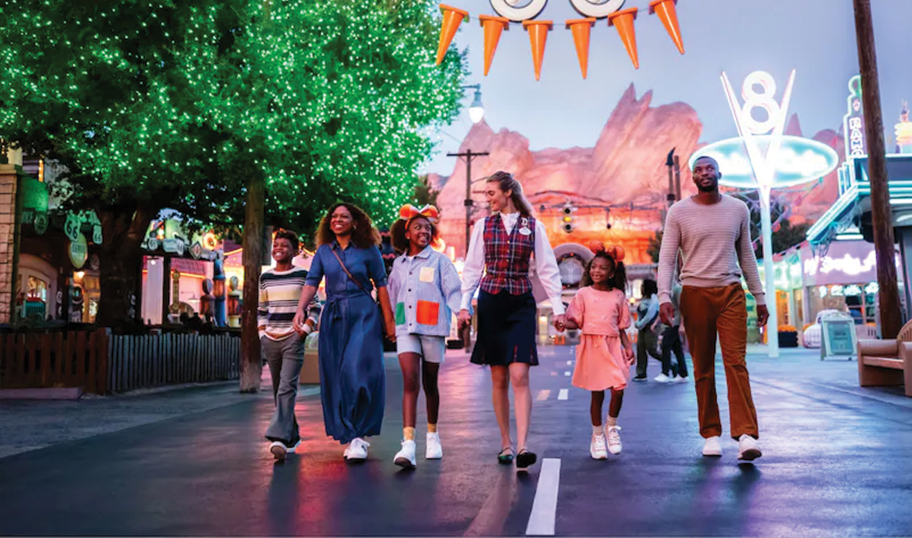A family and a guide walk happily down a brightly lit street on Disney VIP Tours