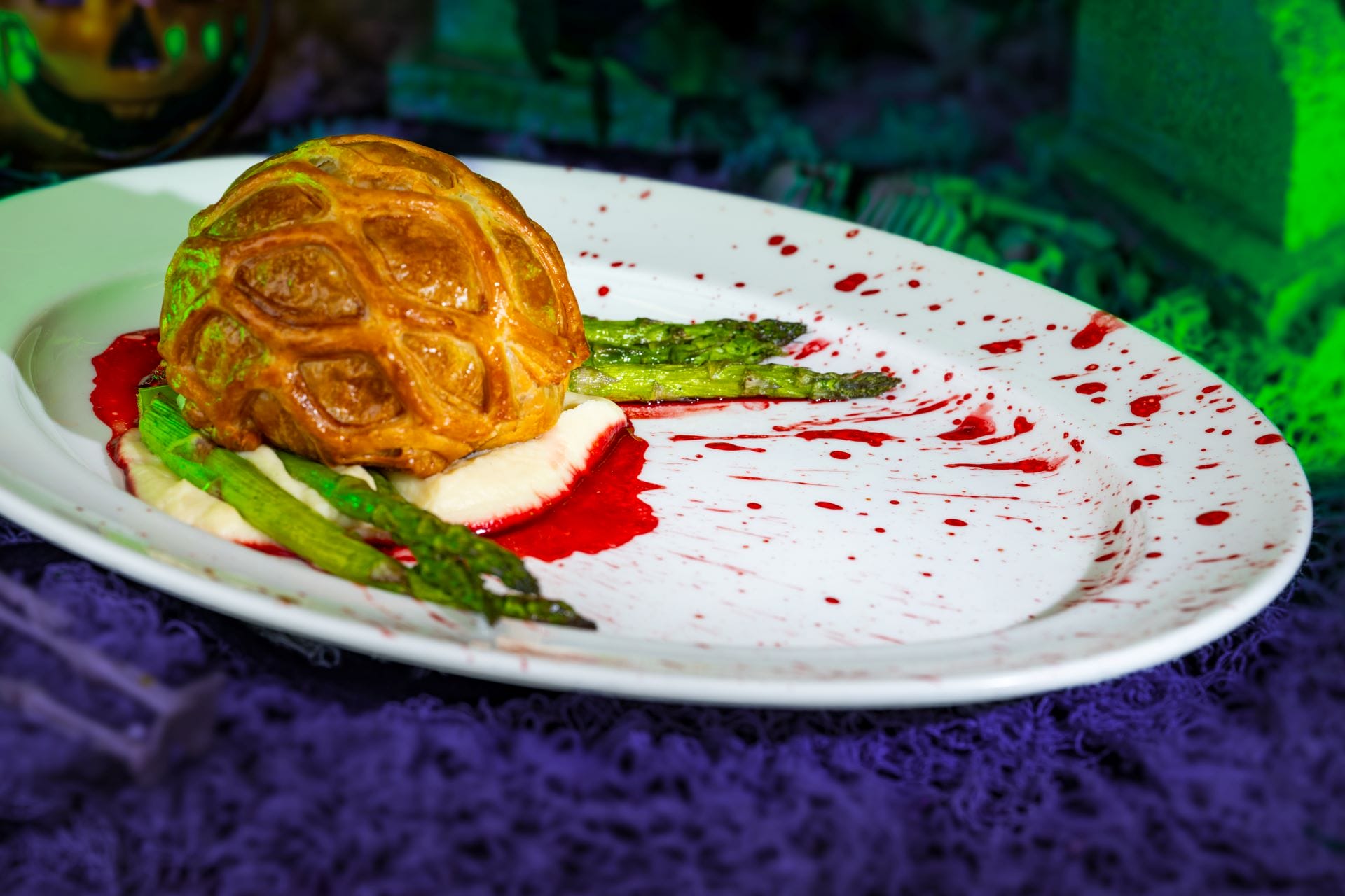 A gourmet pastry atop sauce and asparagus, plated with red splatters, perfect for 2025 food and beverages.