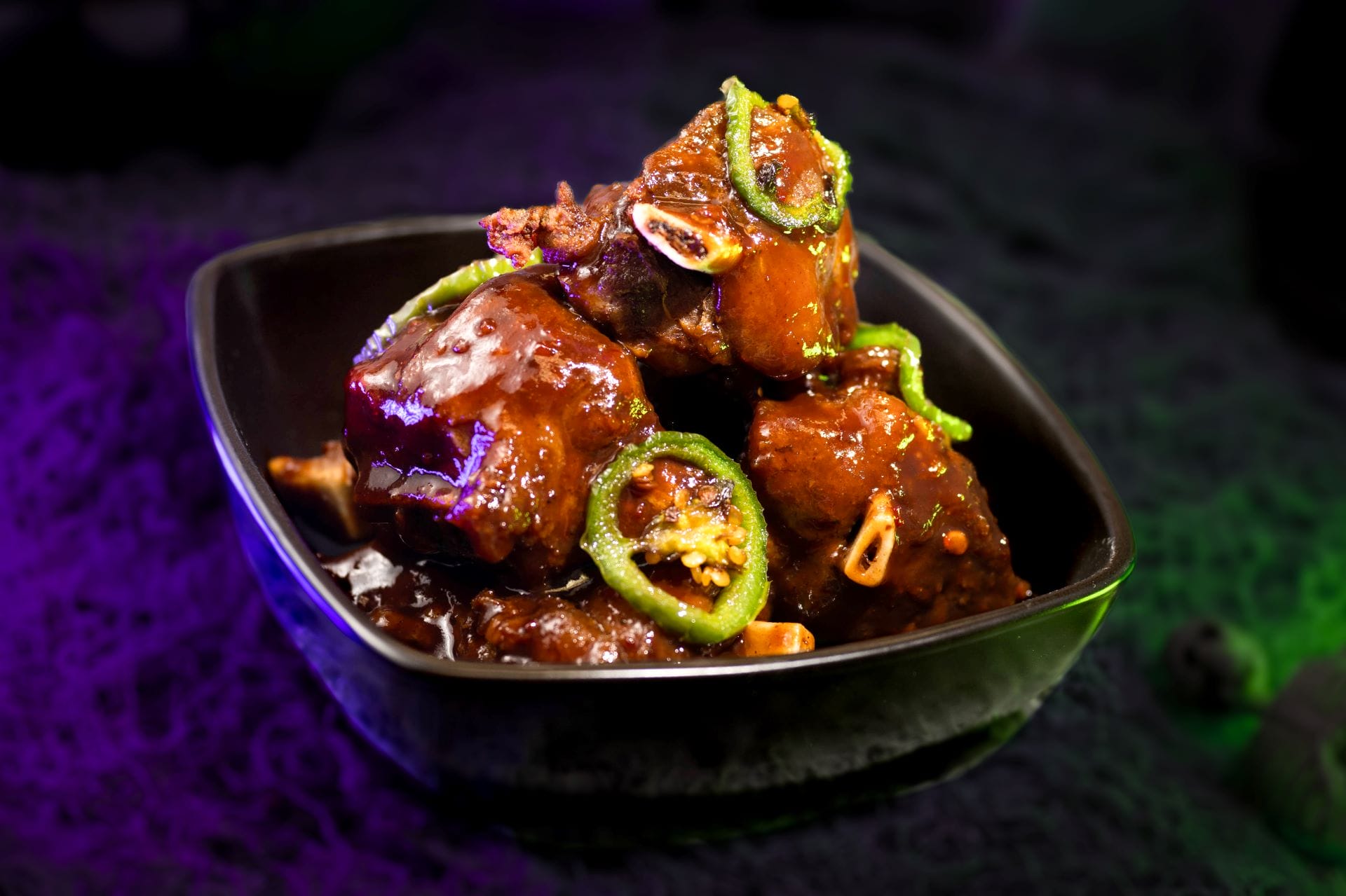 A bowl of glazed meat pieces garnished with green chilies, perfect for food and beverages at Mickey's Not So Scary Halloween Party.