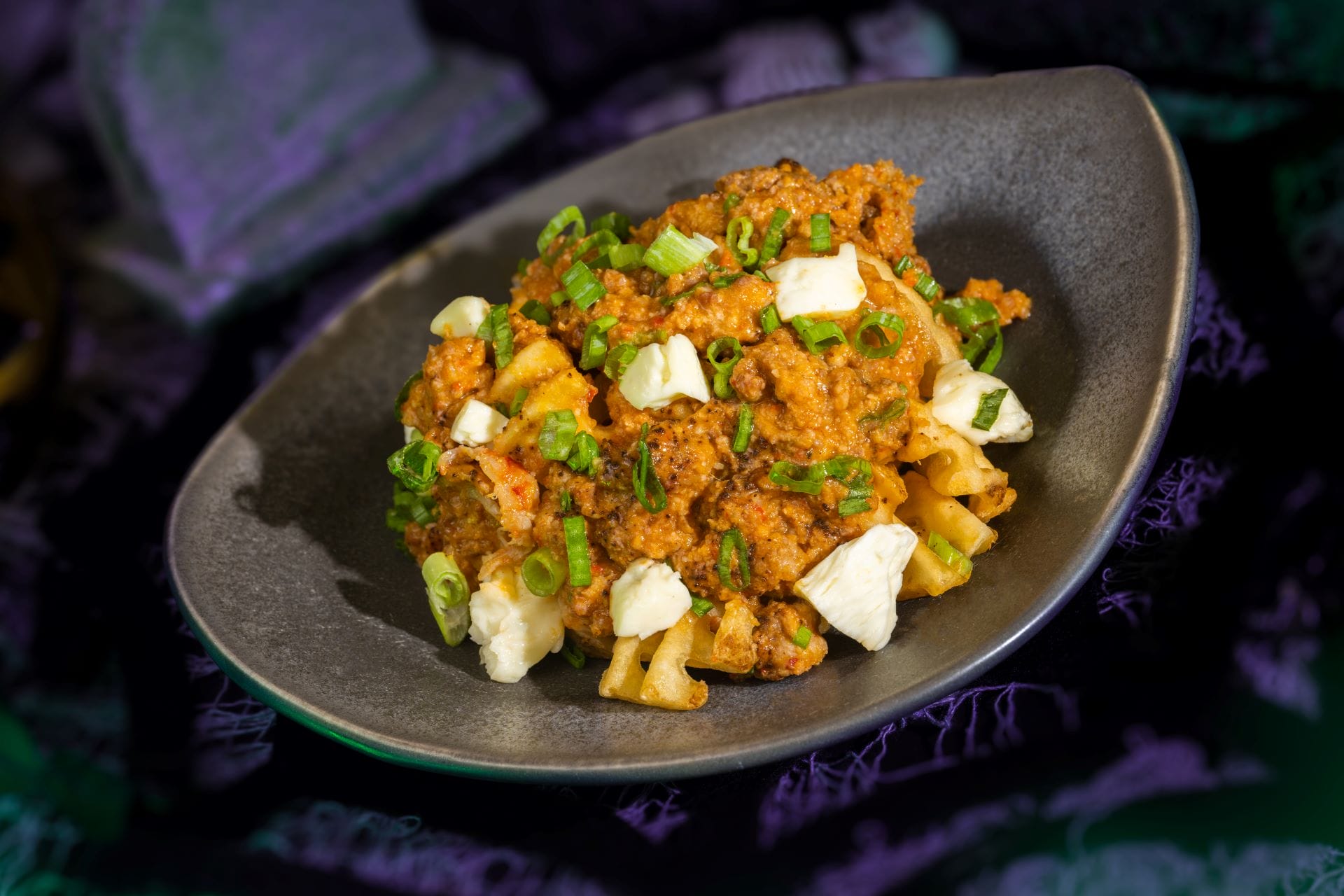 A bowl of macaroni topped with ground meat sauce, diced white cheese, and chopped green onions at this food event.