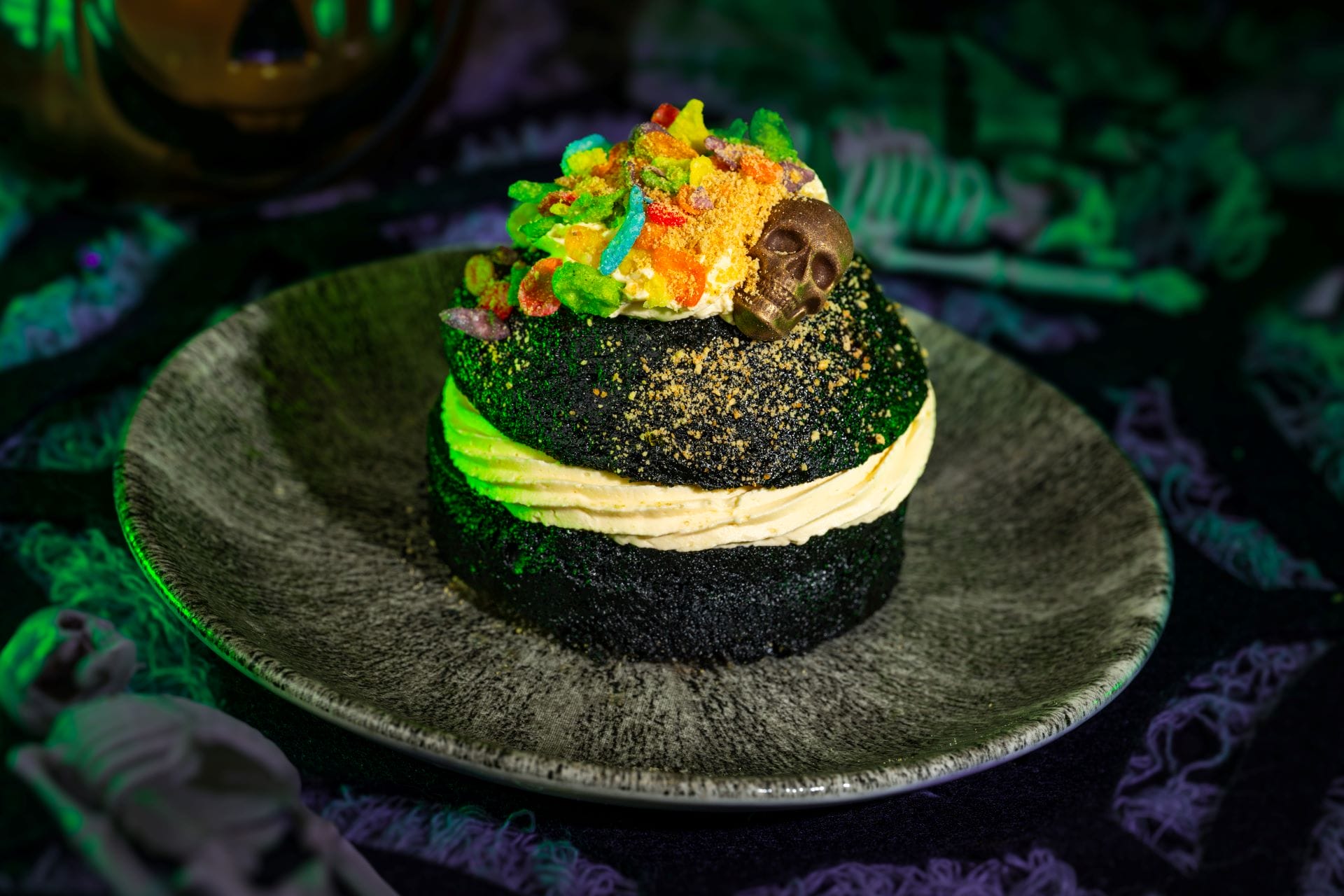 A black cupcake with yellow frosting and rainbow cereal, inspired by Mickey's Not So Scary Halloween Party, on a spooky plate.