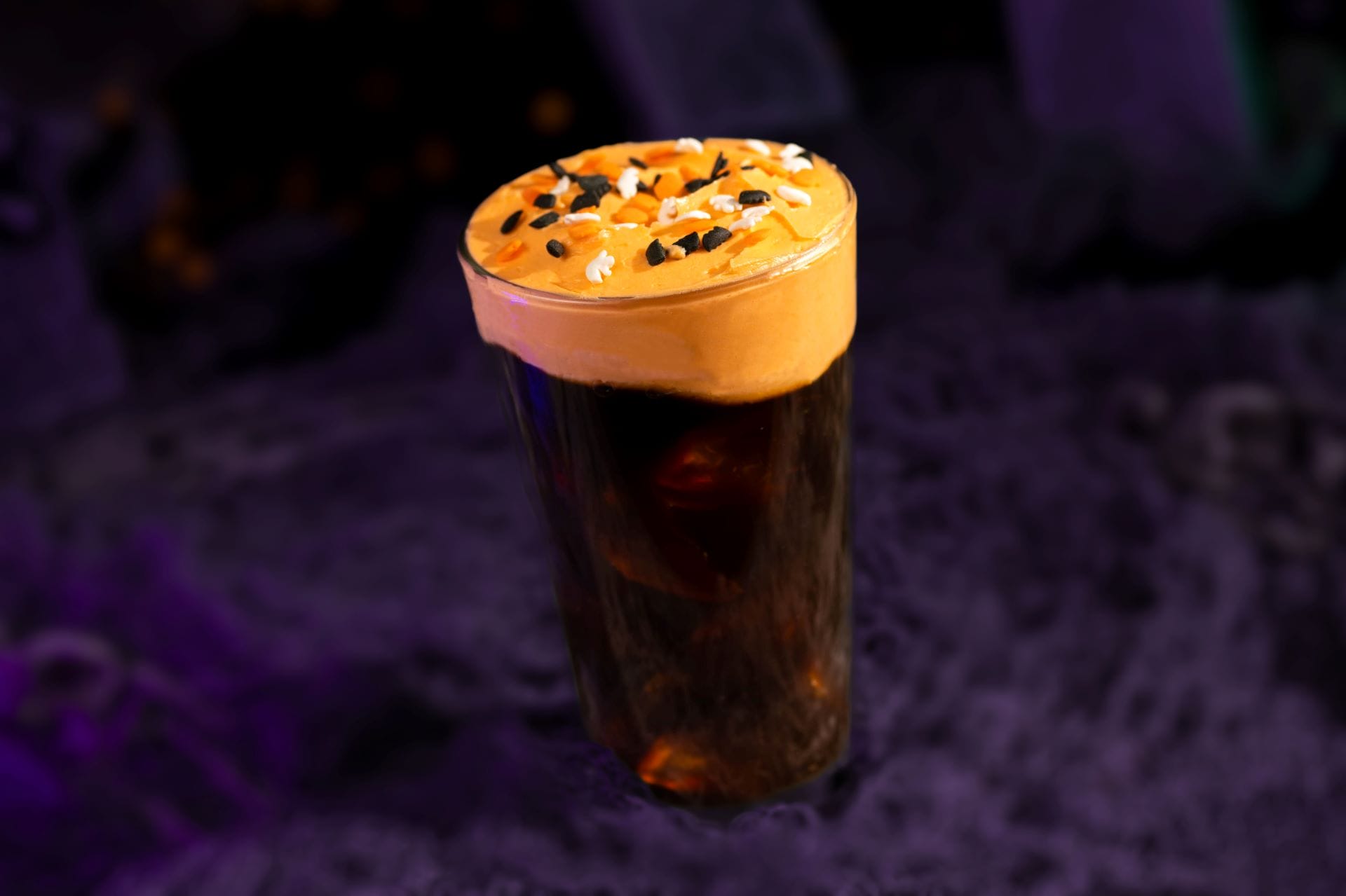 A glass of dark soda with orange whipped topping, perfect for Mickey's Not So Scary Halloween Party in 2025.