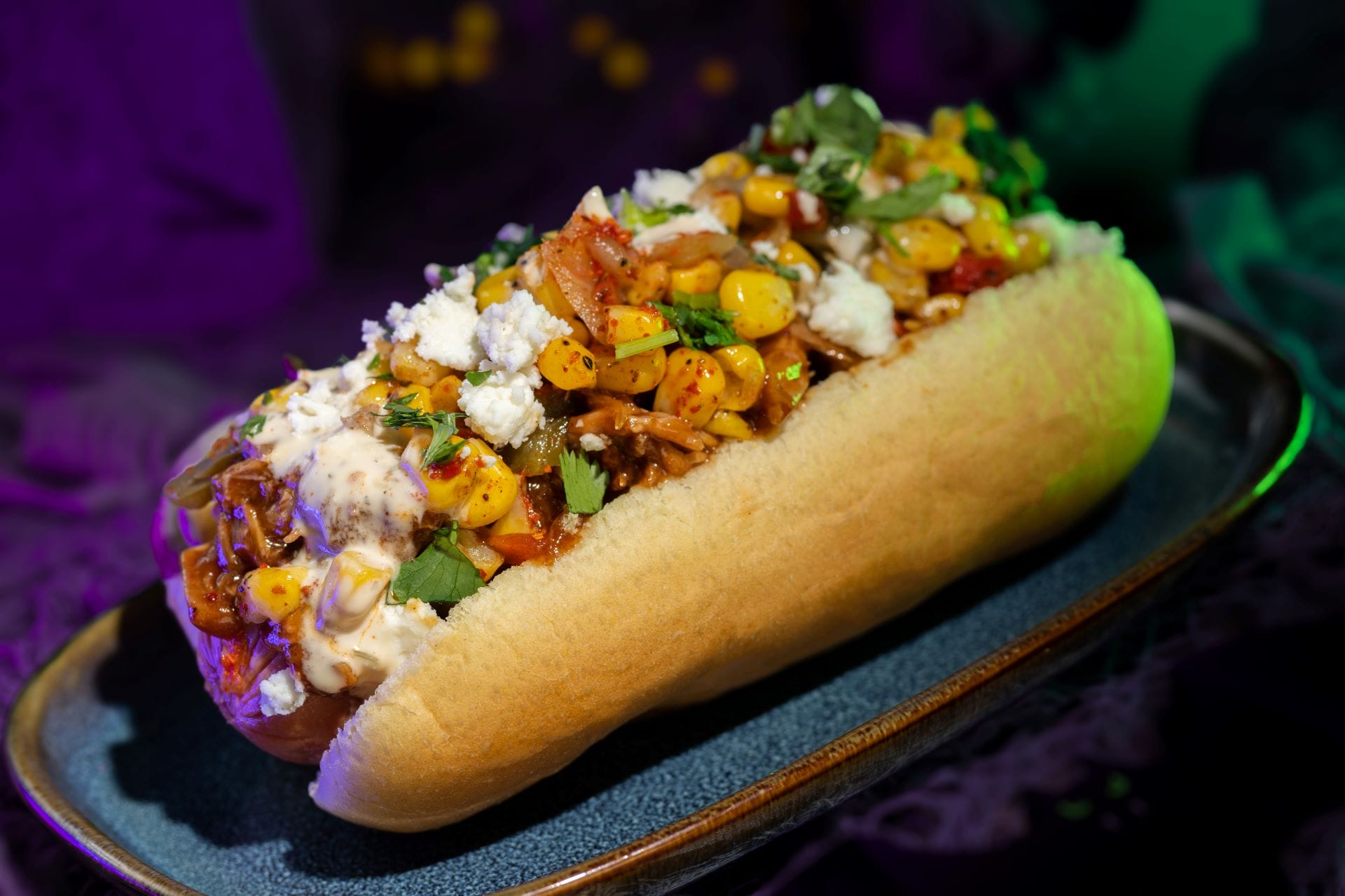 A hot dog topped with corn, cheese, and herbs—perfect 2025 food and beverages for Mickey's Not So Scary Halloween Party.