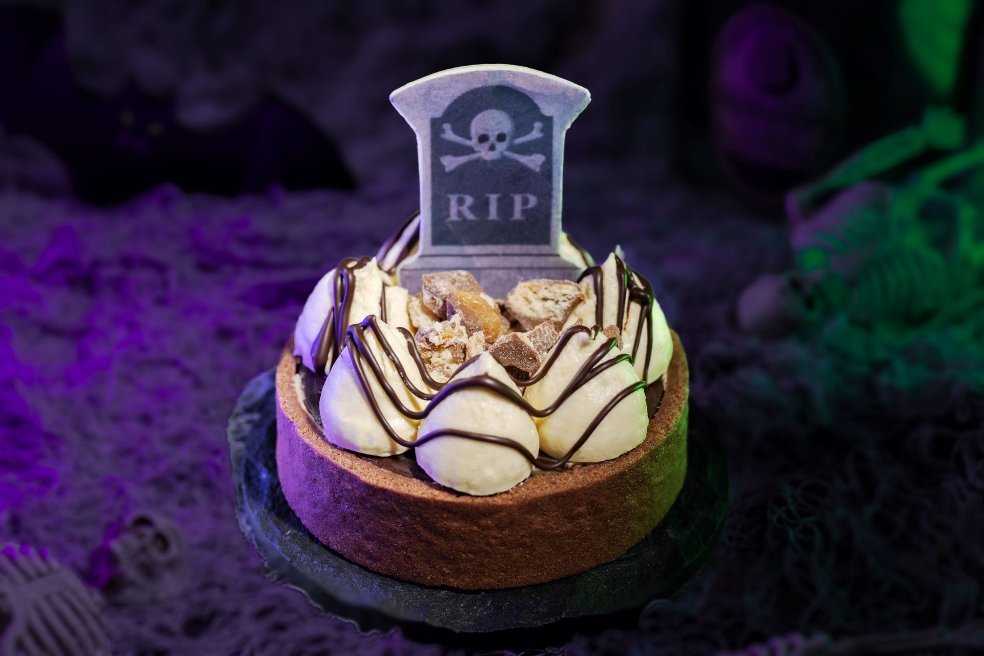 A 2025 Halloween tart with cream, chocolate drizzle, and a "RIP" tombstone cookie at Mickey's Not So Scary Halloween Party.