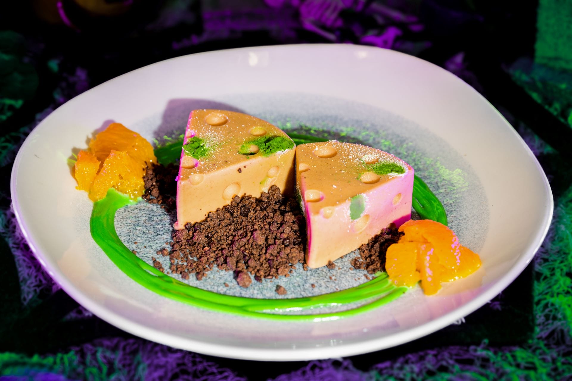 Two triangular mousse desserts on a white plate at Mickey's Not So Scary Halloween Party, with green sauce and orange fruit.