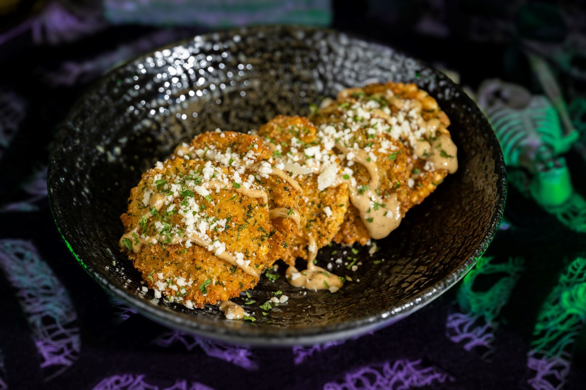 Three breaded fried green tomato slices drizzled with sauce—a 2025 food and beverages treat at Mickey's Not So Scary Halloween Party.