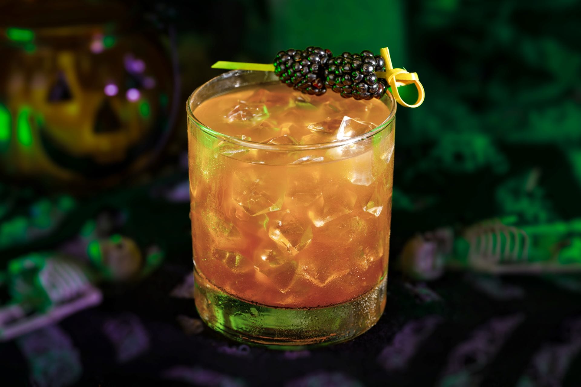 A cocktail with ice and two blackberries on a pick, perfect for 2025's Mickey's Not So Scary Halloween Party.