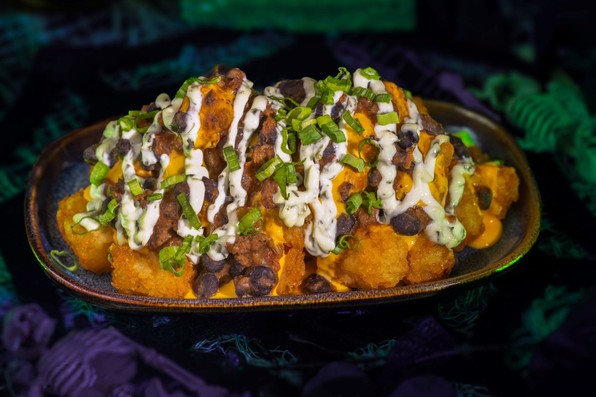A plate of loaded tater tots topped with cheese, ground beef, black beans, and sauce—perfect party food.