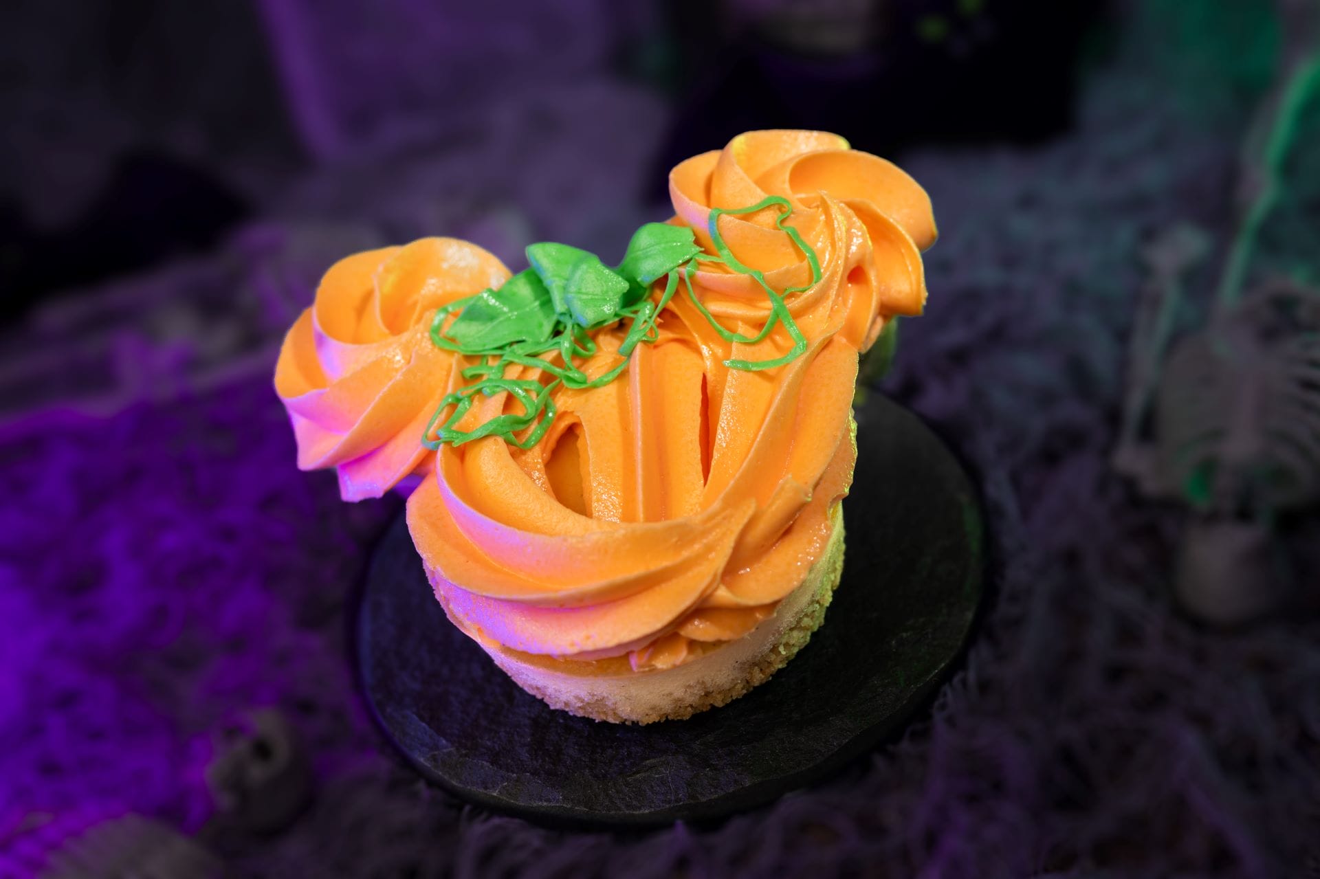 A pumpkin-shaped cupcake with orange frosting, perfect for 2025 Mickey's Not So Scary Halloween Party food and beverages.