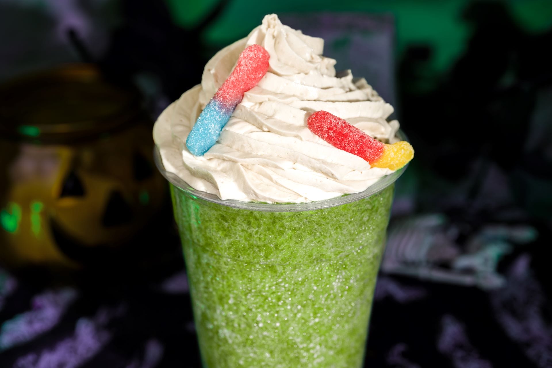 A green slushy beverage topped with whipped cream and gummy worms, inspired by Mickey's Not So Scary Halloween Party.