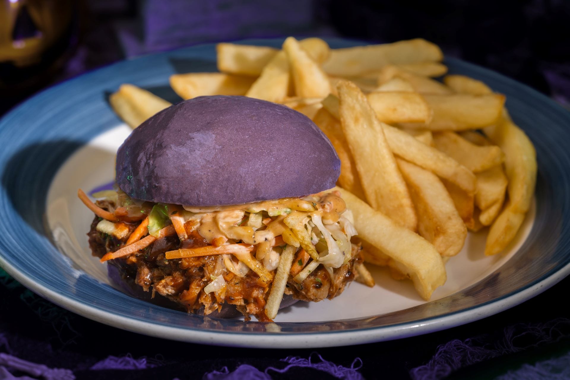A spooky burger with a purple bun, coleslaw, and fries—perfect festive food for Mickey's Not So Scary Halloween Party!
