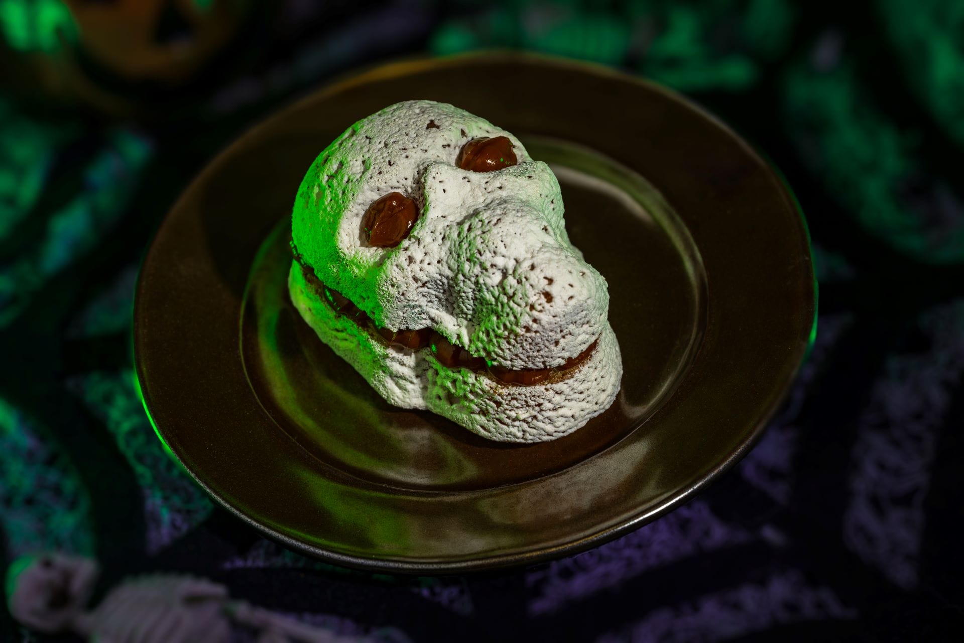 A skull-shaped dessert with chocolate eyes glows on a dark plate at Mickey's Not So Scary Halloween Party 2025.