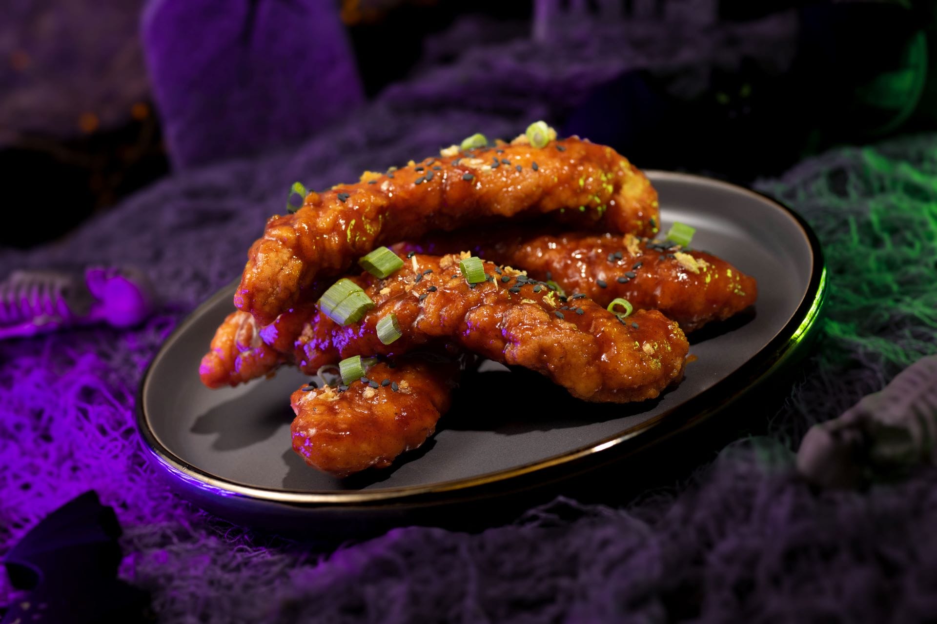 Four crispy glazed chicken tenders at Mickey's Not So Scary Halloween Party 2025, glowing in eerie purple lighting.