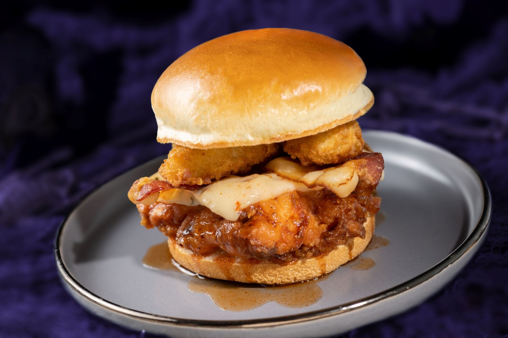 A 2025 food and beverages favorite: fried chicken sandwich with cheese, bacon, and sauce on a bun.