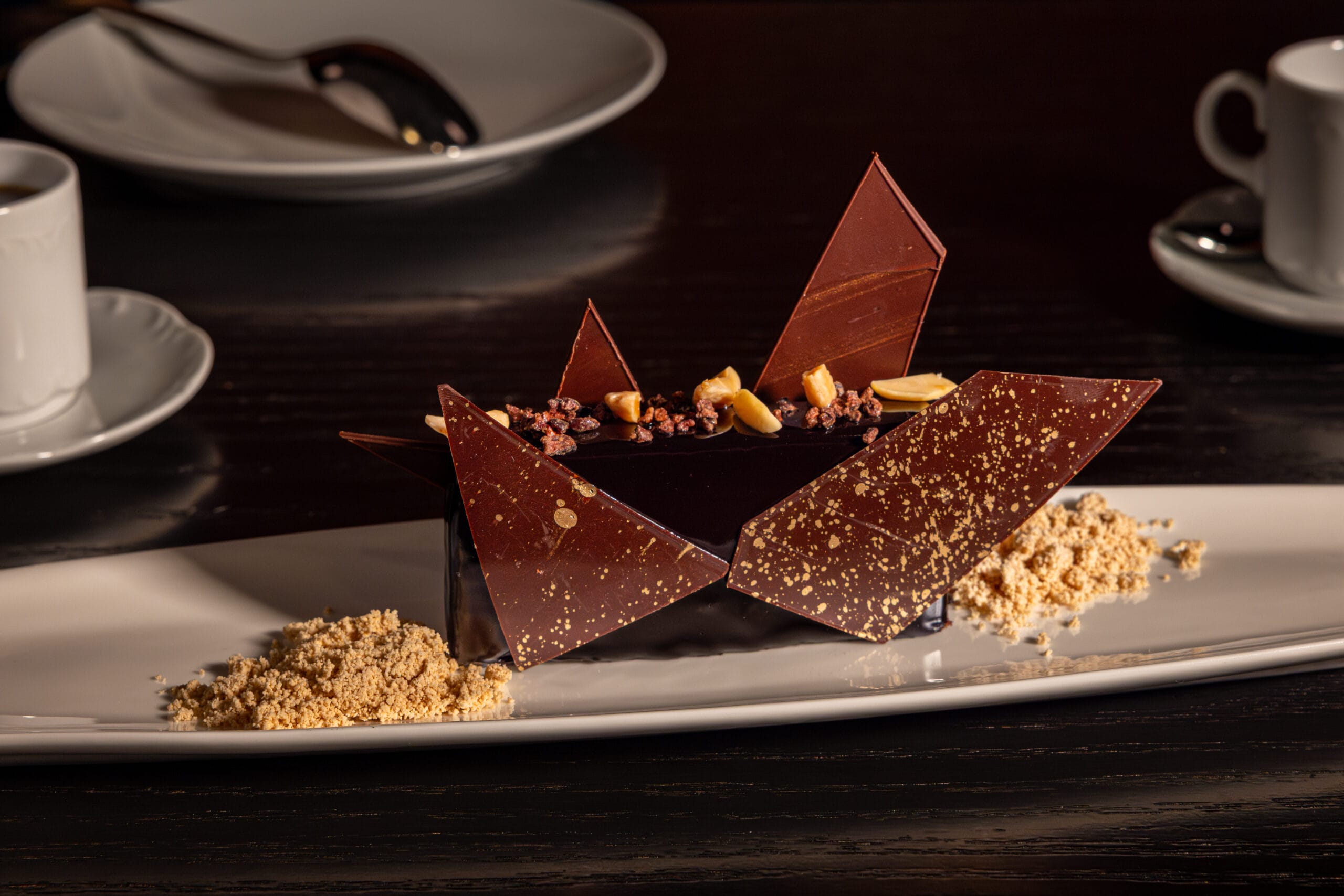 Plated chocolate dessert at Bourbon Steak, with shards and nuts, served on white dish near coffee cups at the Dolphin Hotel.