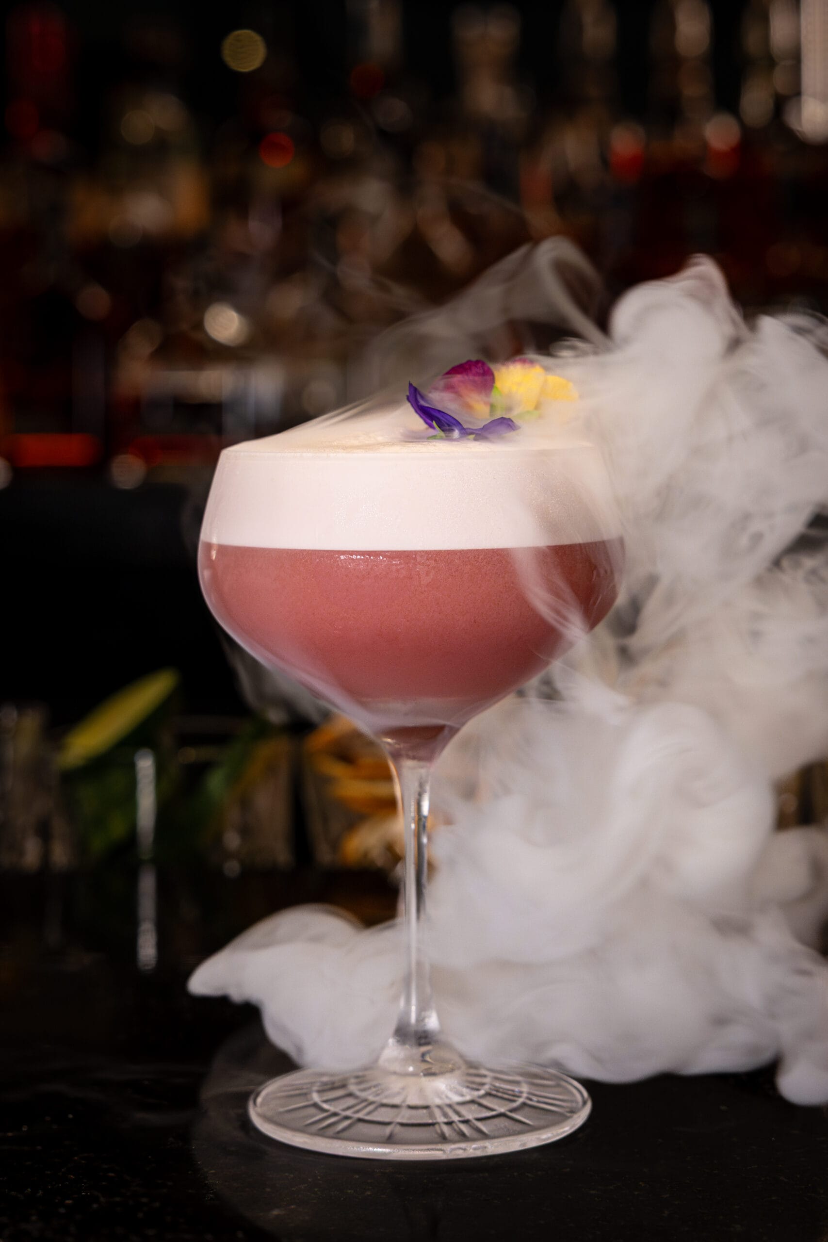A pink cocktail in a coupe glass with foam at Bourbon Steak, Walt Disney World Dolphin Hotel, garnished with flowers.