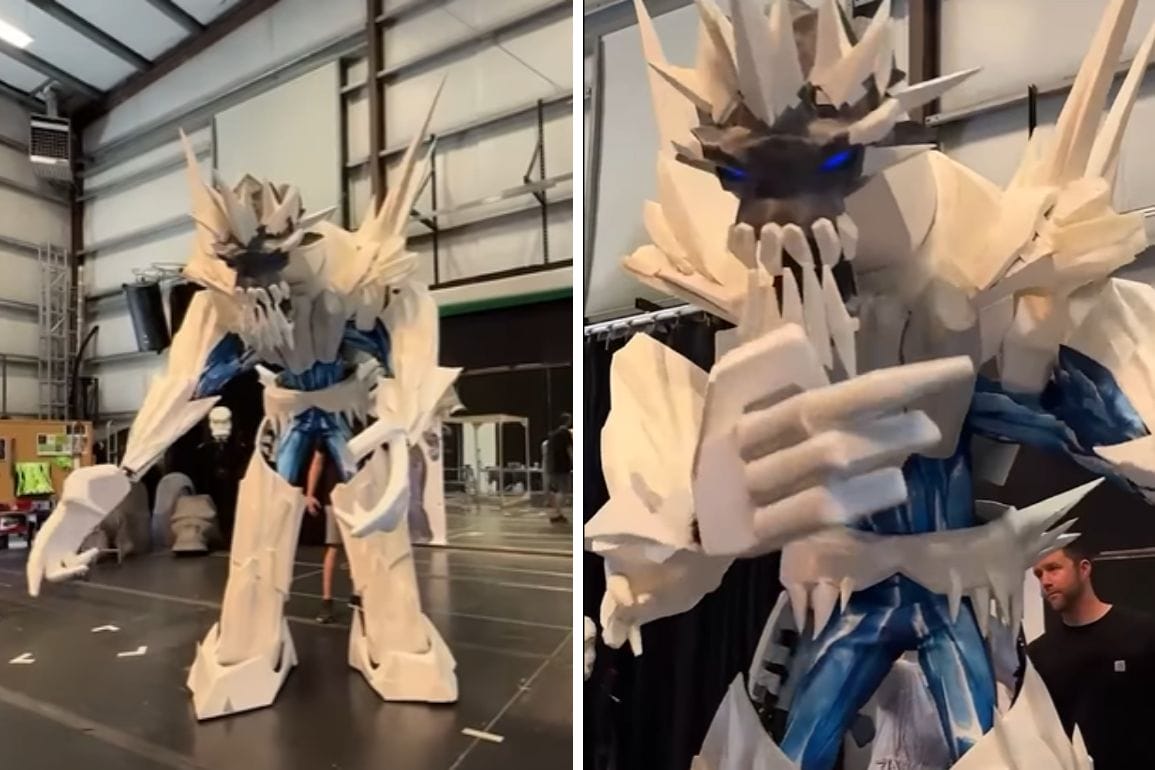 A person wears a large, spiky Titan Puppet costume with blue details, standing in an indoor studio space.