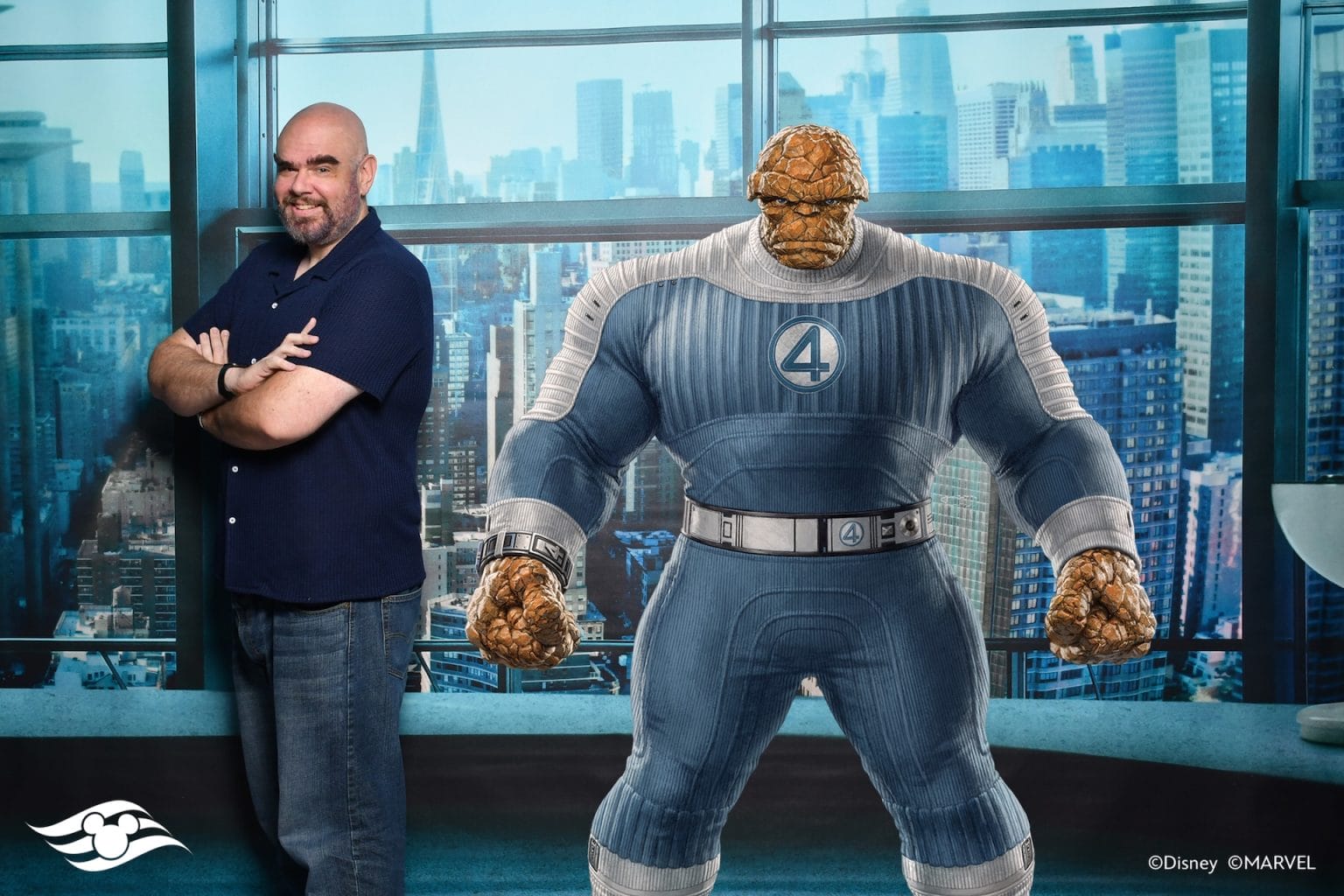 A man smiles by a life-sized Fantastic Four Magic Shot image of The Thing, set against a cityscape backdrop.